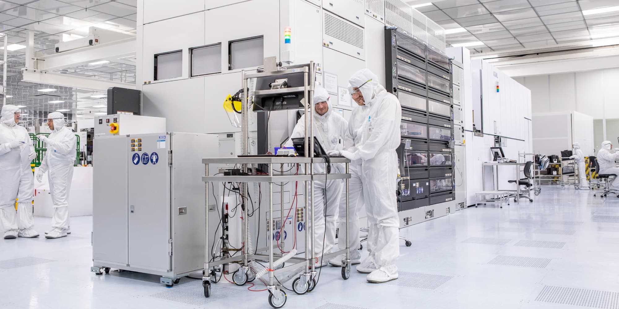 Collaborative-research Researchers in cleanroom suits collaborating beside semiconductor equipment in a cleanroom