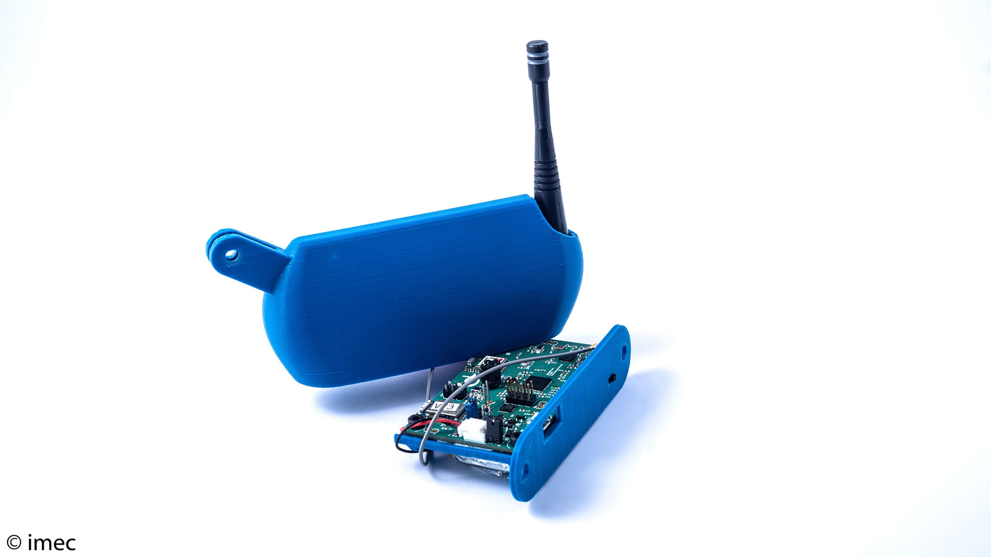 Conamo001_1 Blauwe 3D-geprinte sensorbehuizing met blootliggende printplaat en antenne op een witte achtergrond