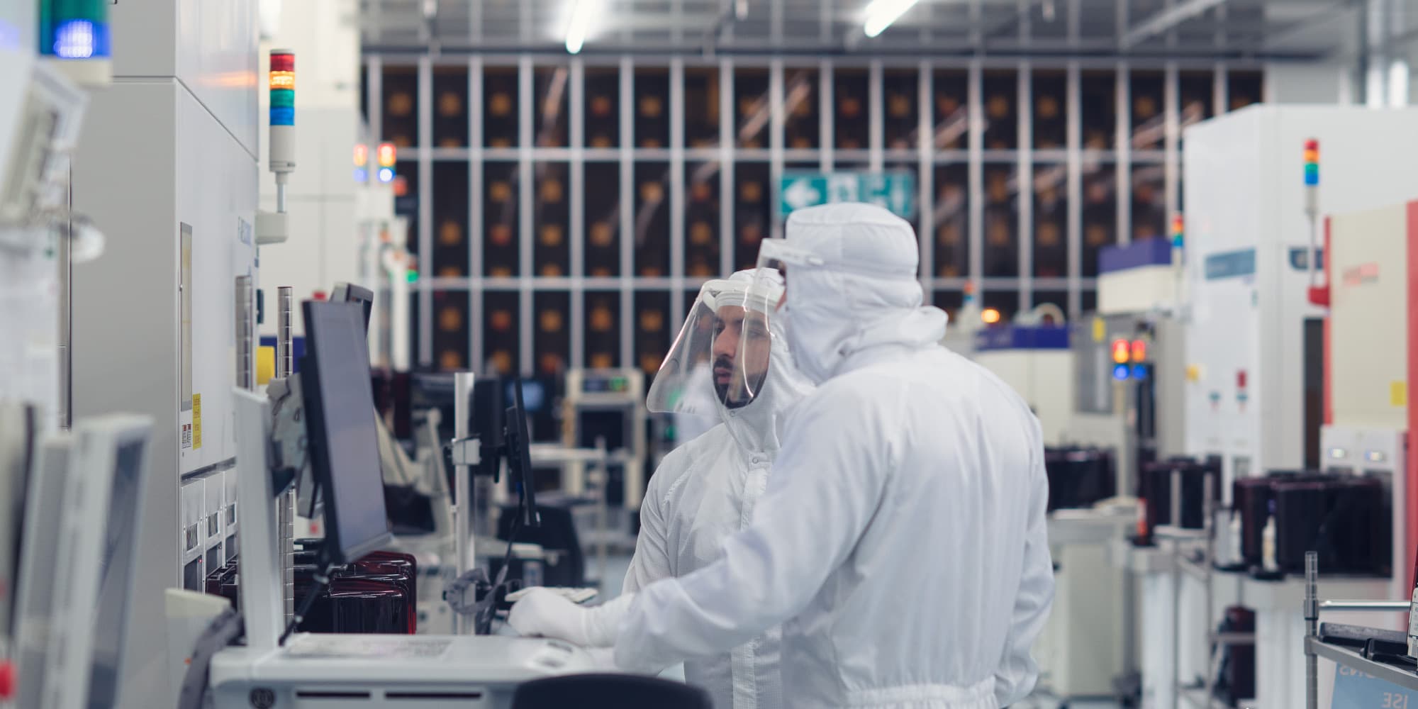 Connect-technology-centers Two cleanroom technicians in white suits reviewing a monitor in a semiconductor lab