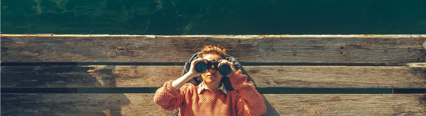 coverbeeld_knip_1 Person holding binoculars while looking over a wooden railing