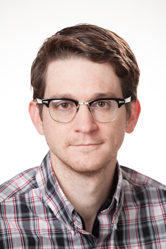 Daniel_Denman_3_1 Head-and-shoulders portrait of Dan Denman wearing glasses and a plaid shirt against a white background.