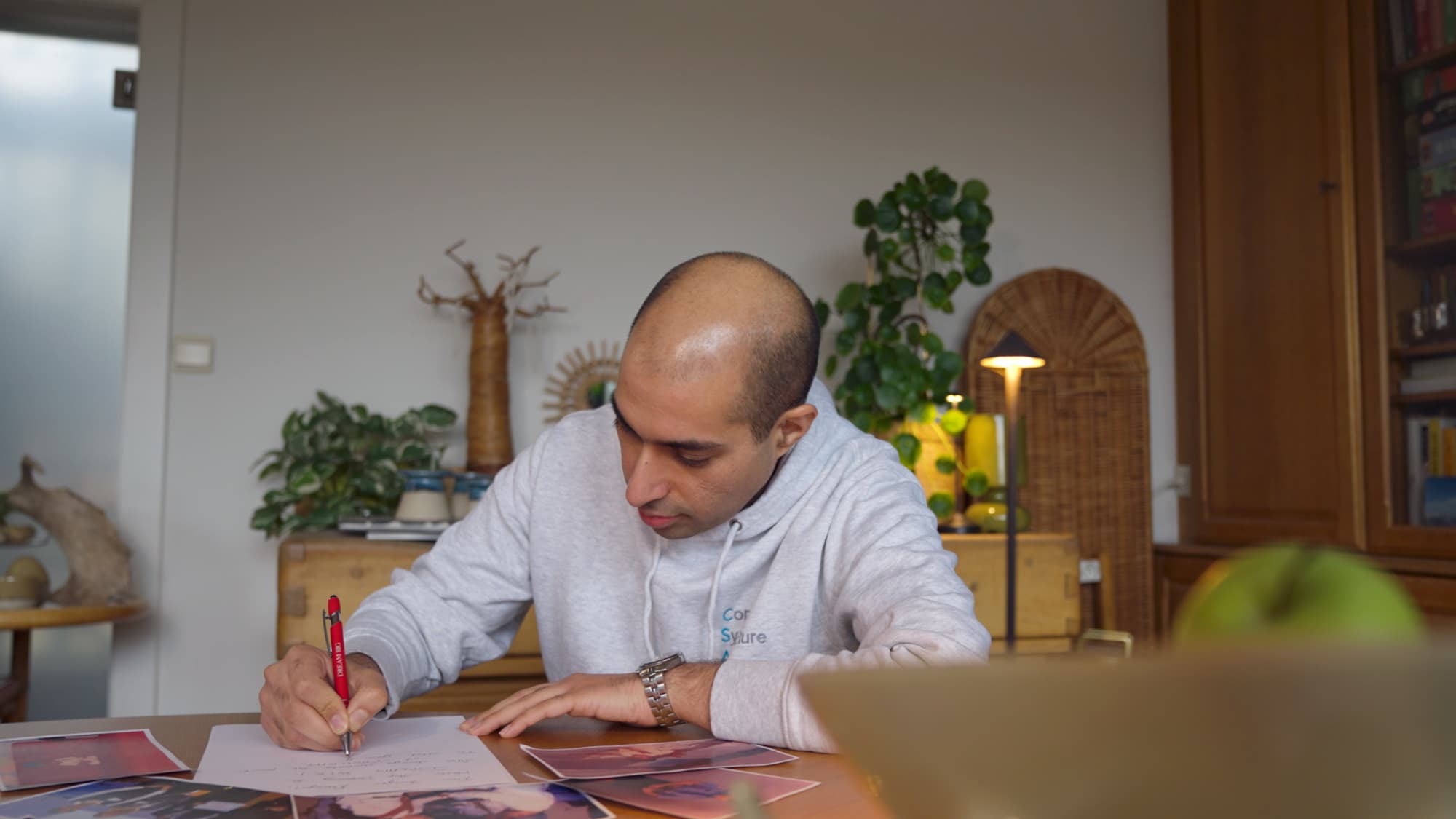 Darayus-Adil-Patel-1 Darayus Adil Patel writing at a table with printed photos spread around him in a home office