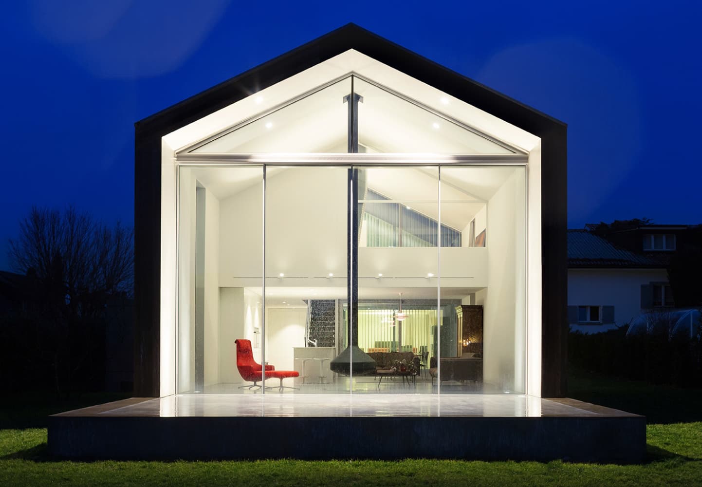 dcnanogrid_1 Modern glass-fronted house lit at night, showing a bright open interior and red chair