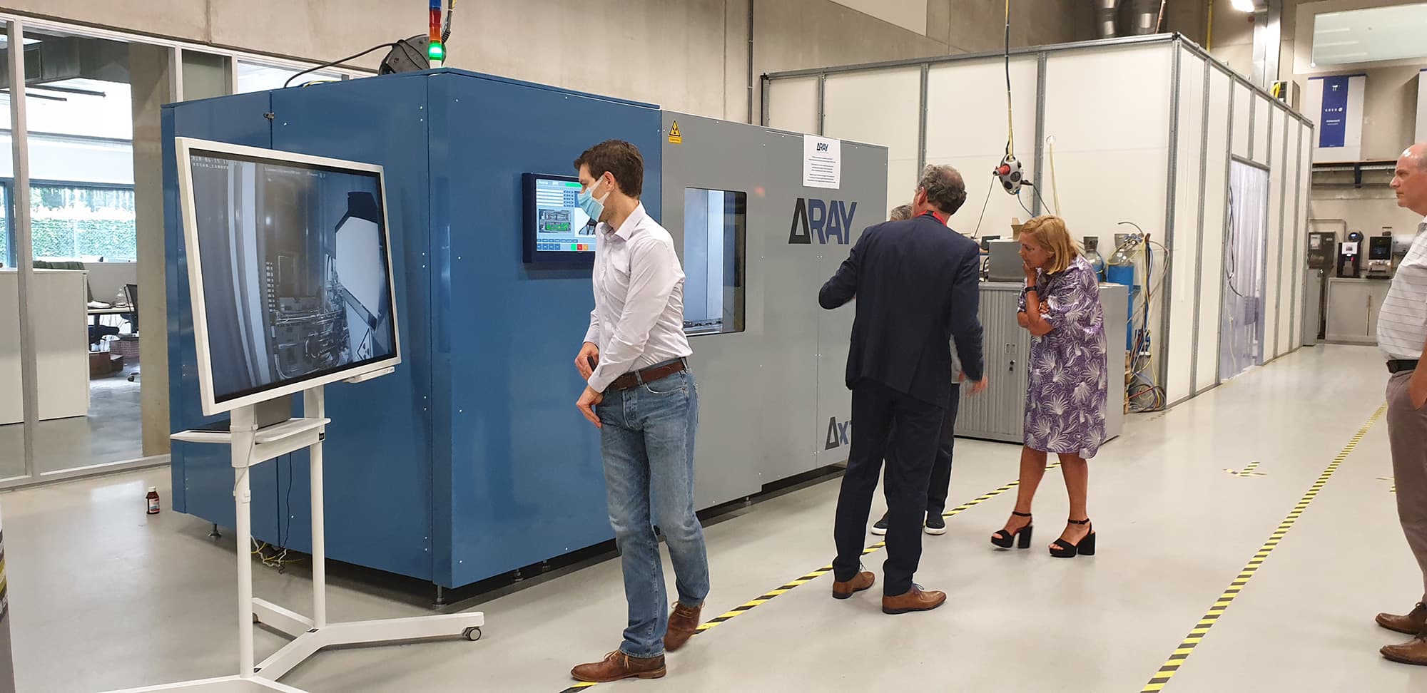 People observing large Deltaray machine in lab People observing a large Deltaray machine in a clean lab, with a monitor displaying its controls