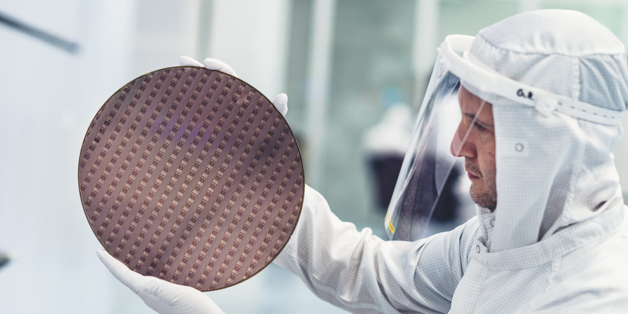 Development Researcher in a cleanroom holding a semiconductor wafer