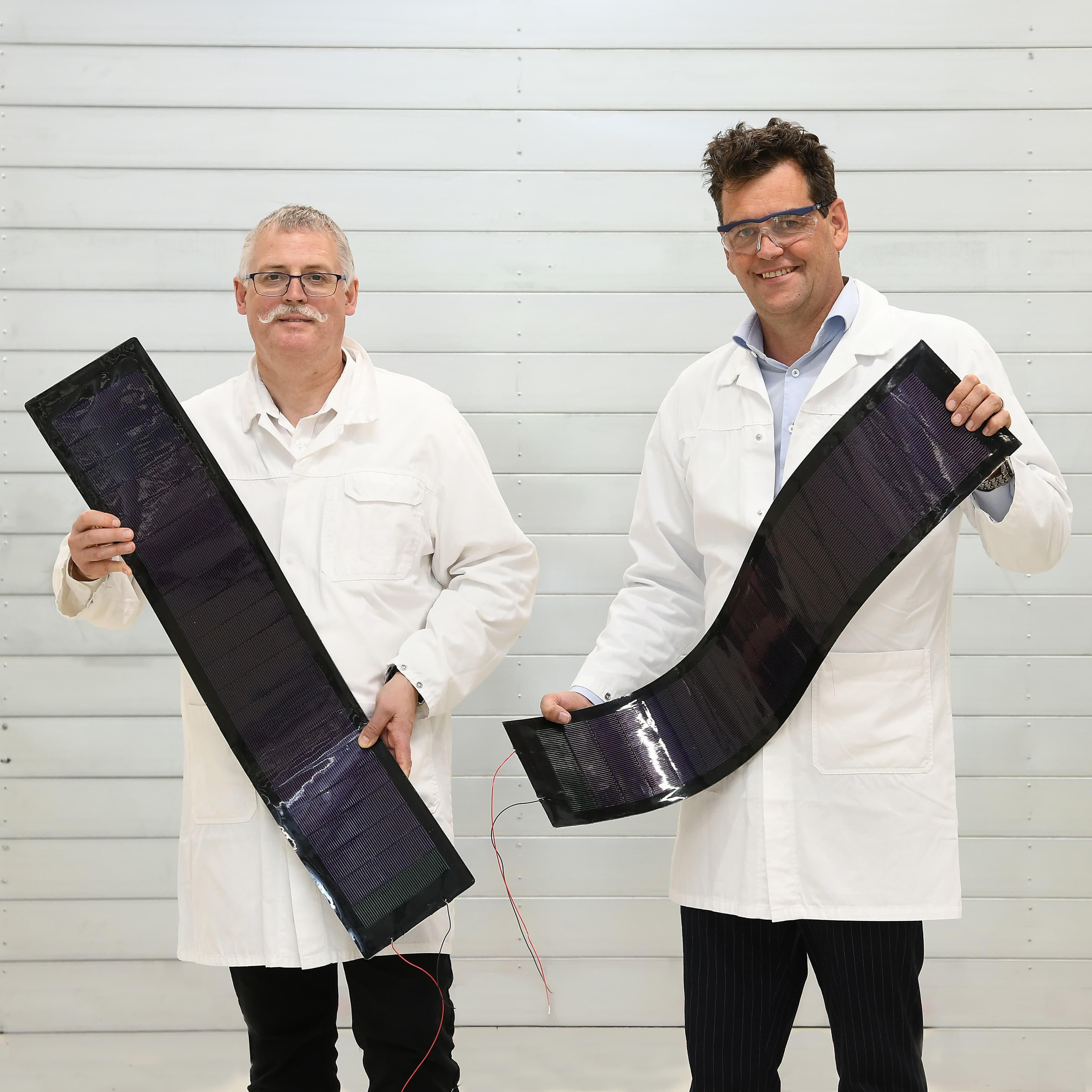DSC_8267 Two researchers in lab coats hold curved flexible solar panels.
