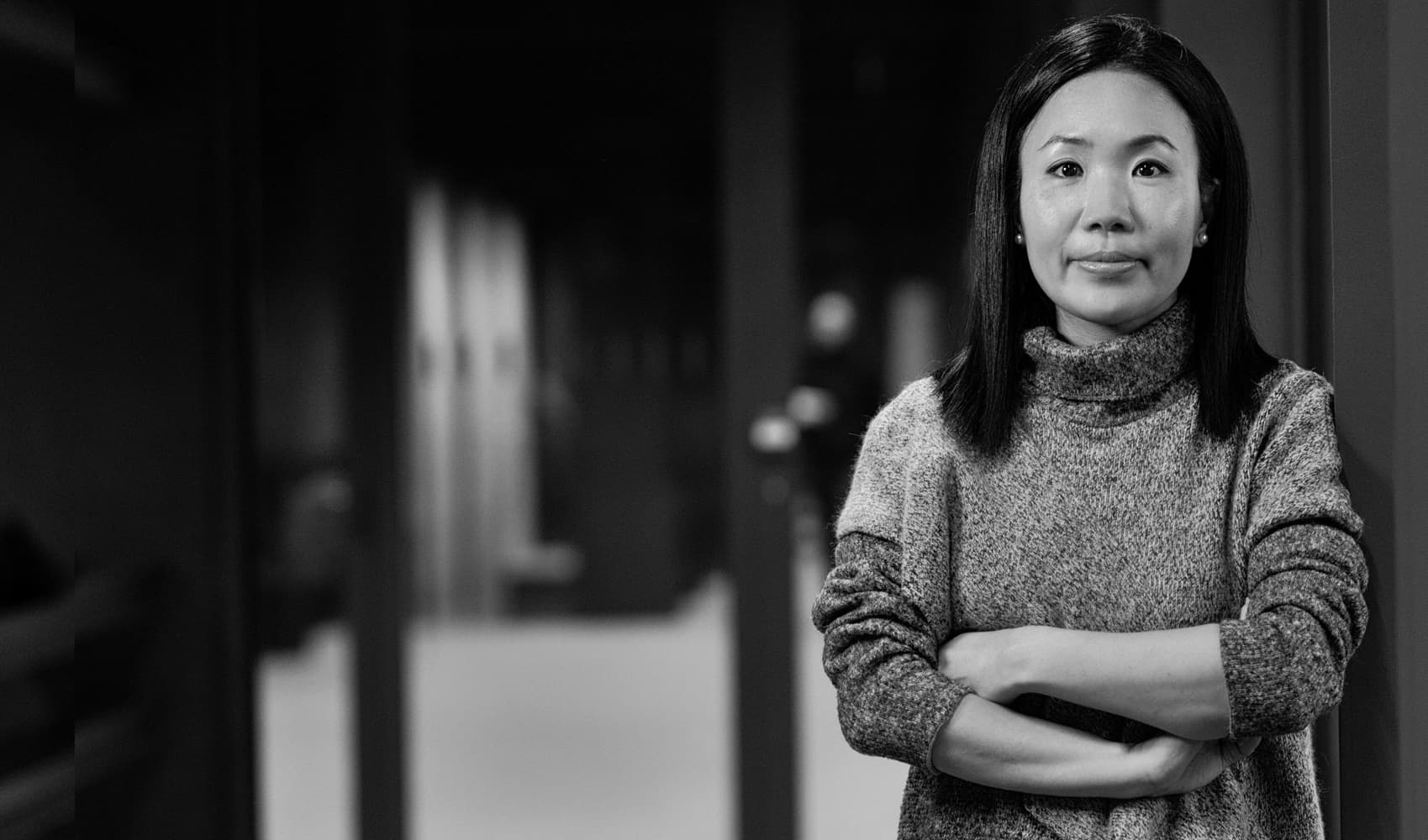 E.Park001magazinenew-_1 Portrait of Jung Yeon Park standing with arms crossed in a hallway, wearing a sweater.