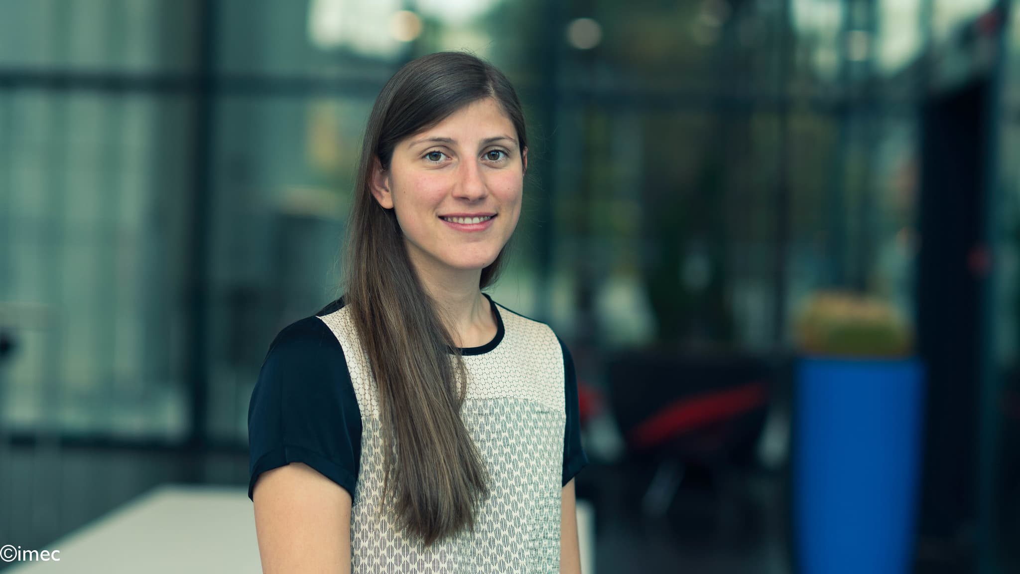 Eline%20Raymenants Portrait of Eline Raymenants, PhD student at imec and KU Leuven, standing indoors with a blurred lab-like background.