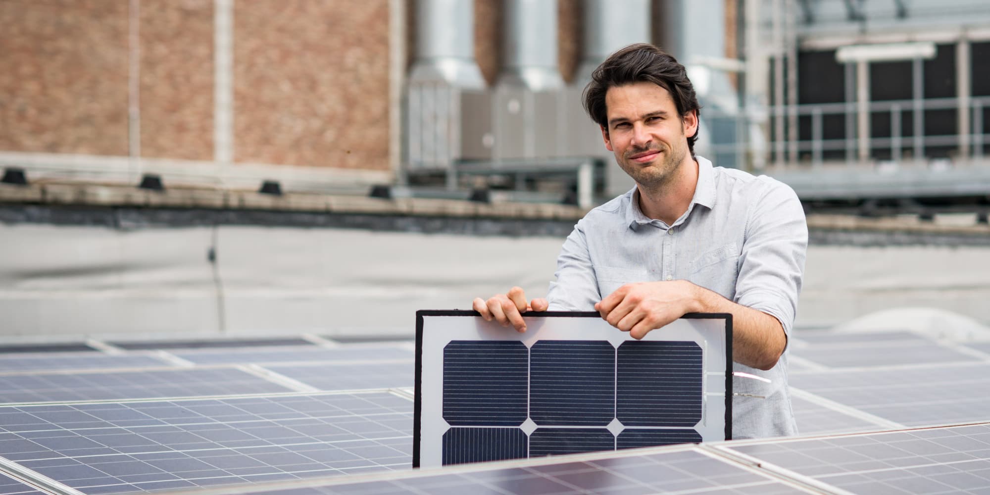 Energy-Yield-Estimation_1 Man standing on a rooftop holding a photovoltaic solar panel above installed solar modules
