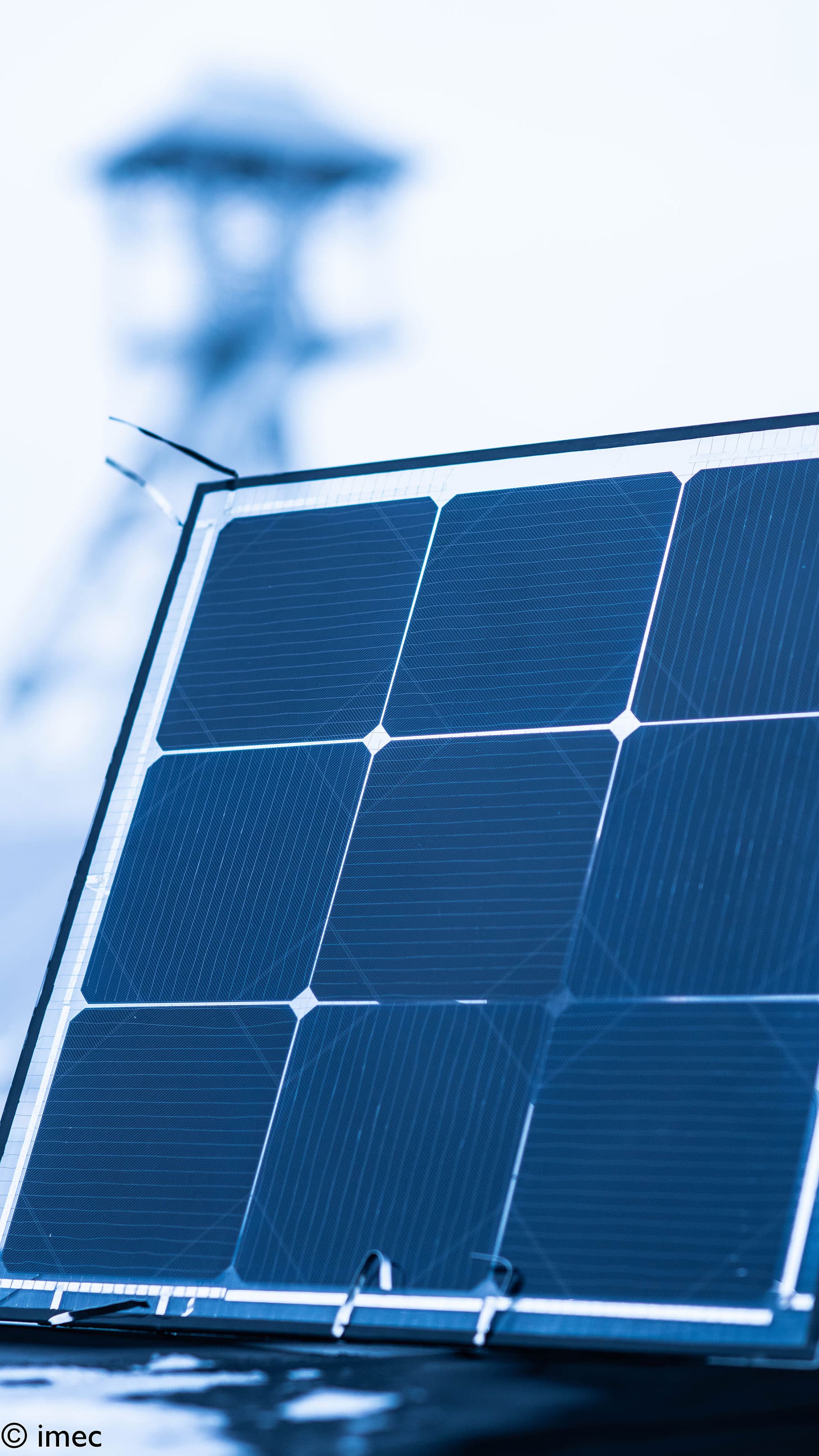 energy-yield-model-bifacial-solarcells002b_1 Close-up of a bifacial solar panel with blue cells and a blurred tower in the background.