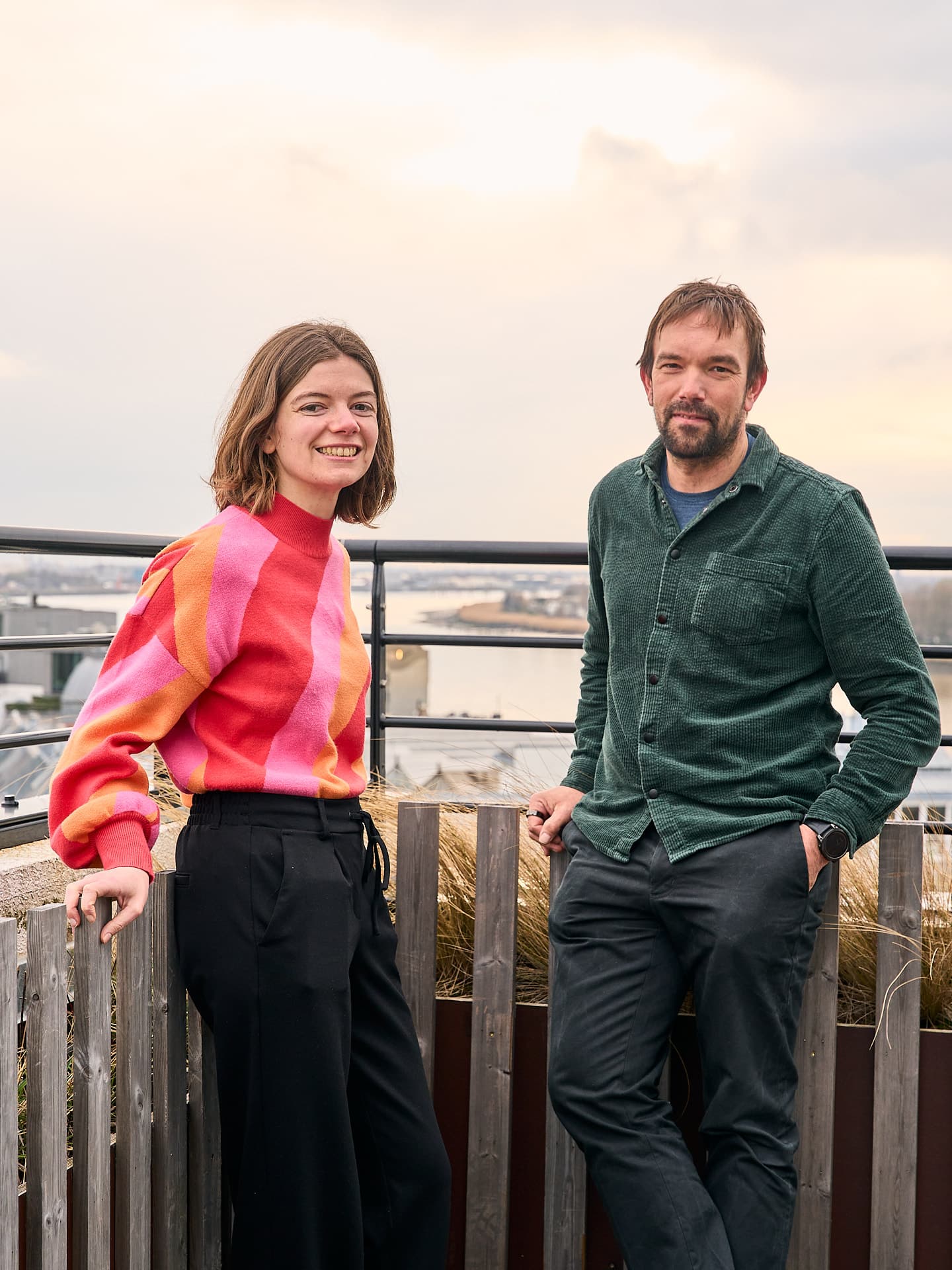 Erika_Lutin-Bart_Nonneman Two people standing on a rooftop terrace, smiling at the camera.