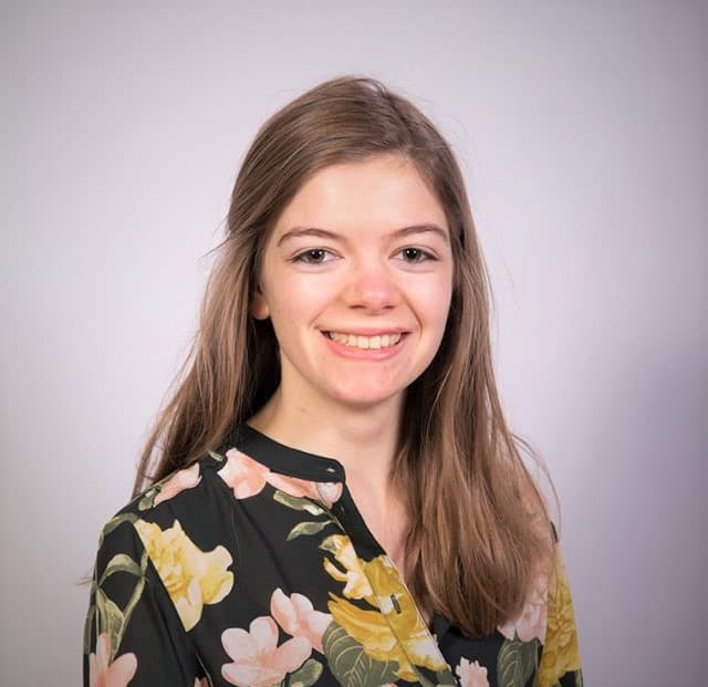 Erika_Lutin_IDpicture_1 Portrait of Erika Lutin smiling in a floral blouse against a light background.