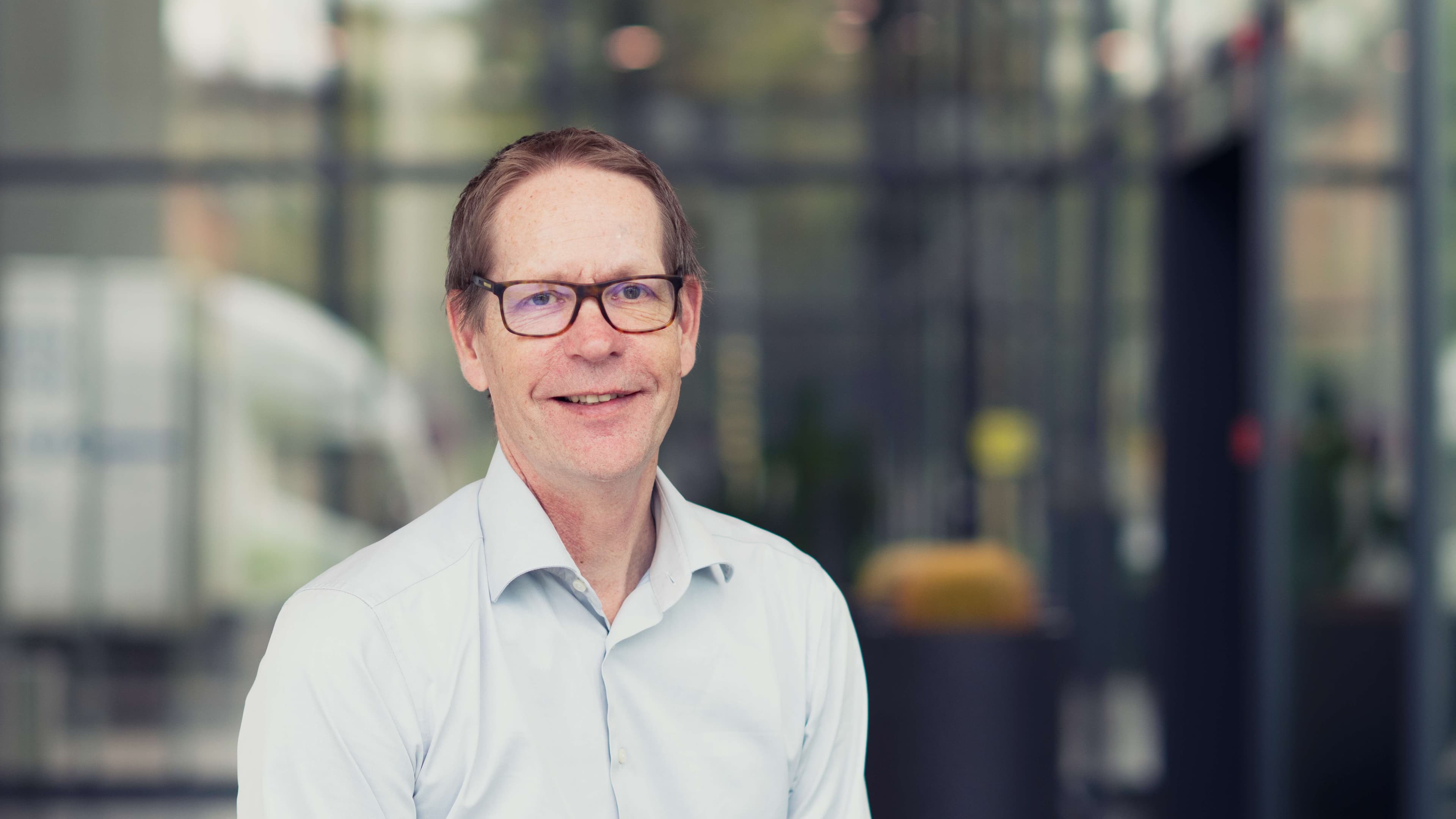 Erwin-Hijzen001 Portrait of Erwin Hijzen, wearing glasses and a white shirt, in front of a blurred lab background