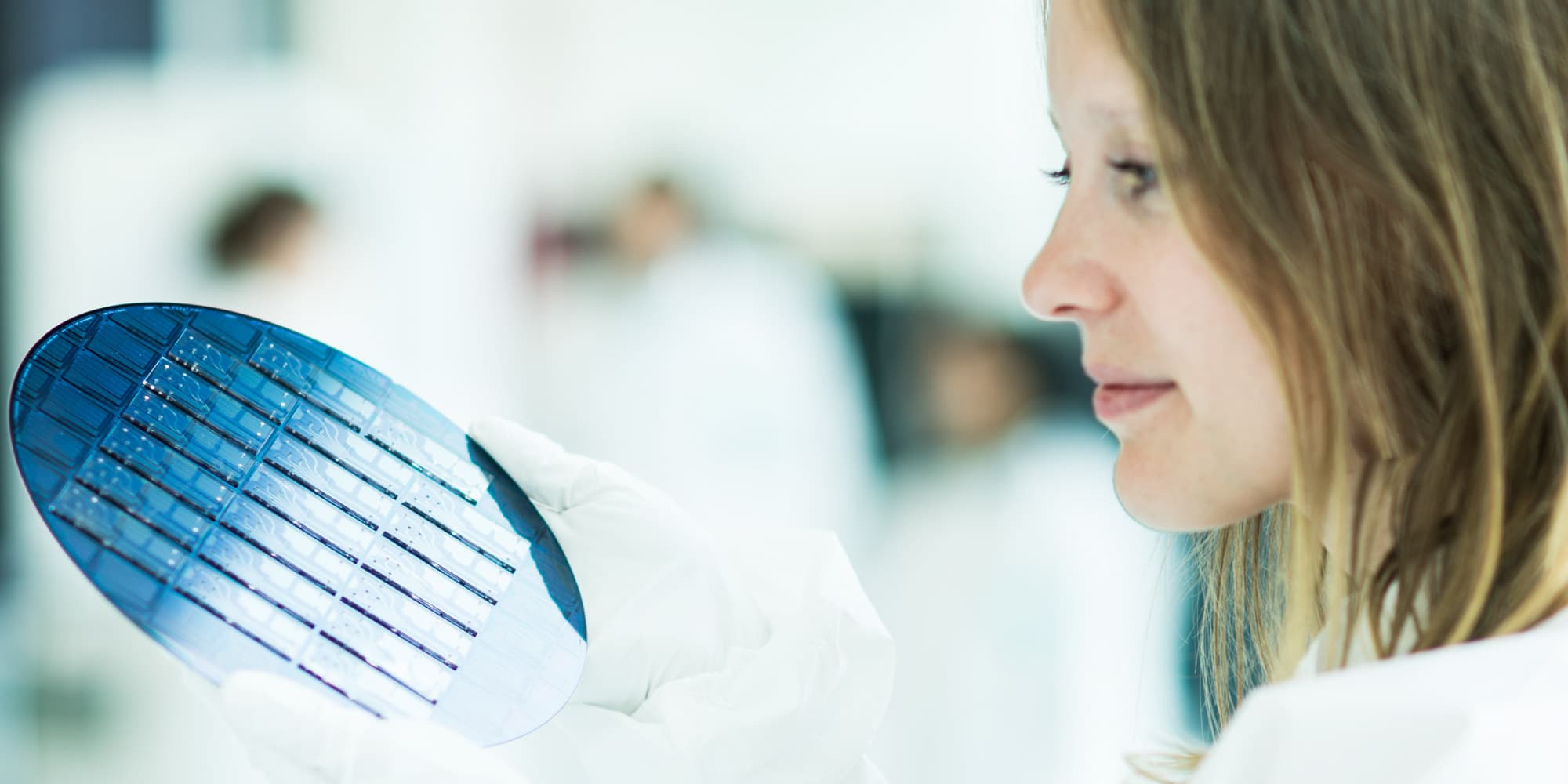 evonetix_3 Researcher examining a blue semiconductor wafer in a cleanroom.