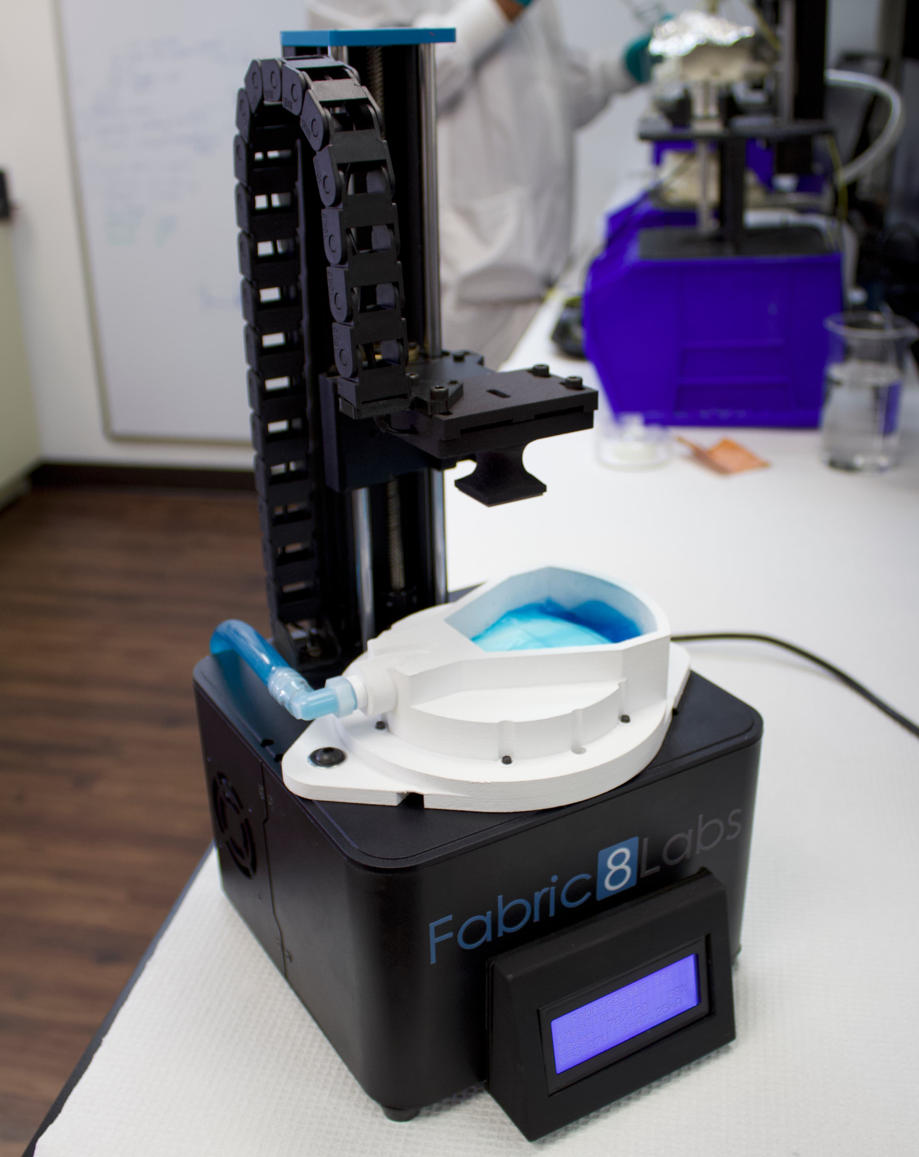 Fabric8Labs prototype 3D metal printer Fabric8Labs-prototype 3D-metaalprinter met een blauw vloeistofbad en zwarte verticale printkop in een laboratorium