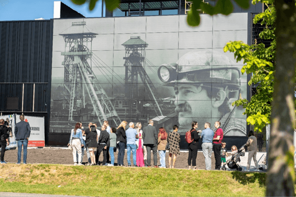 Facade-Soltech Building facade with integrated solar panels and a large industrial mural, with people gathered in front.