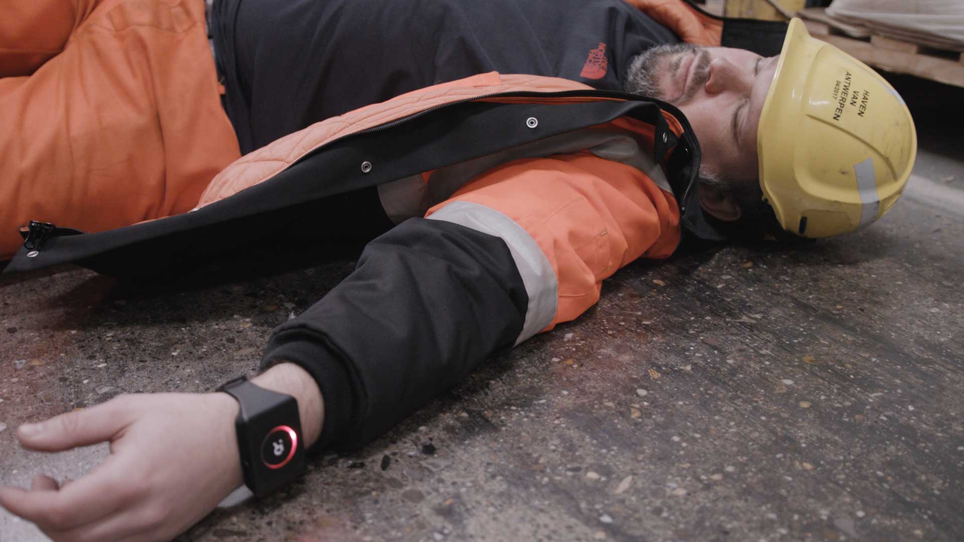 fallen Worker in safety gear lying on the ground, wearing a wrist device with a red alert light