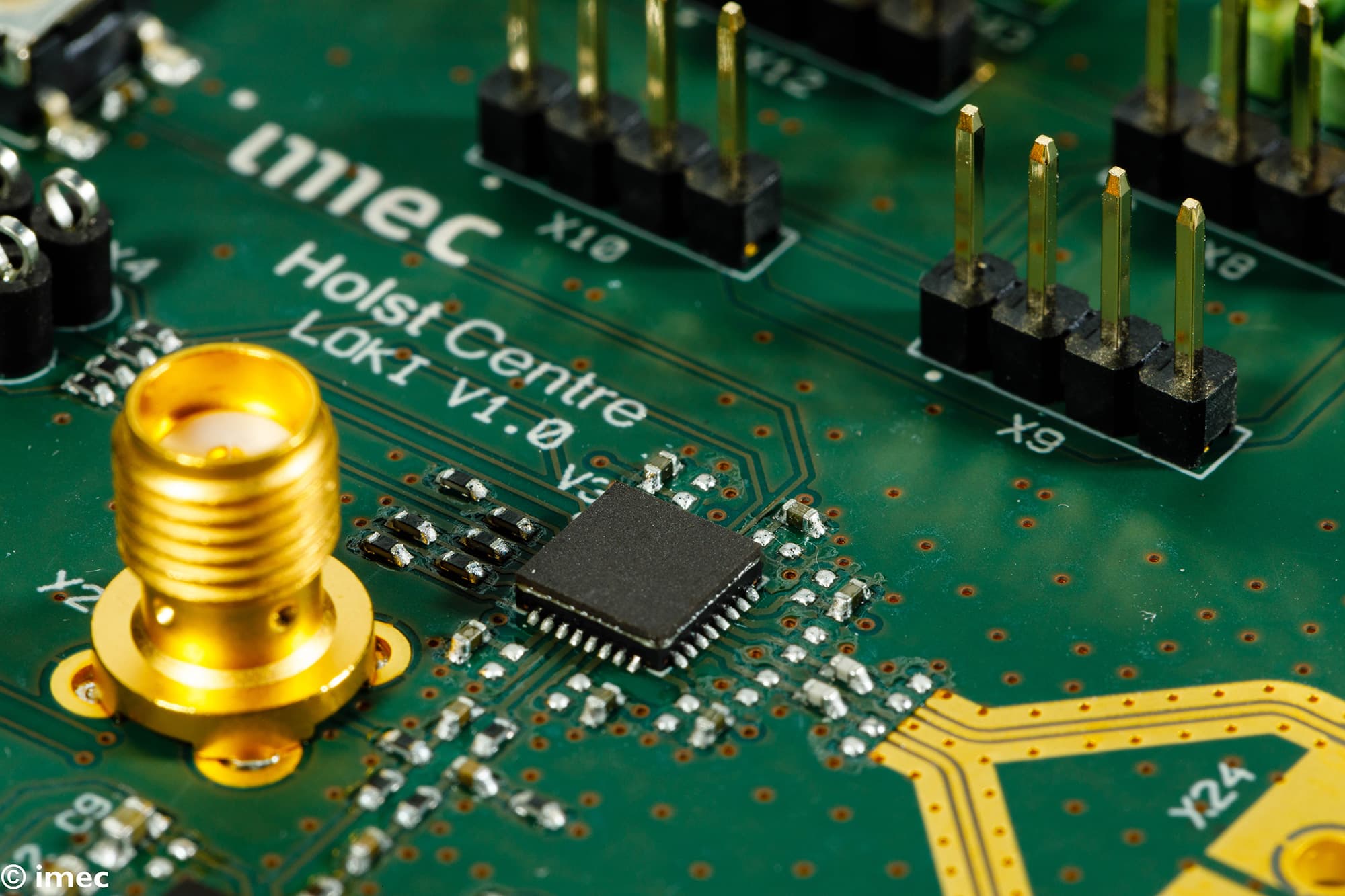 Close-up of a circuit board with imec Holst Centre chip Close-up of a green circuit board with a central chip, gold connectors, and imec Holst Centre markings
