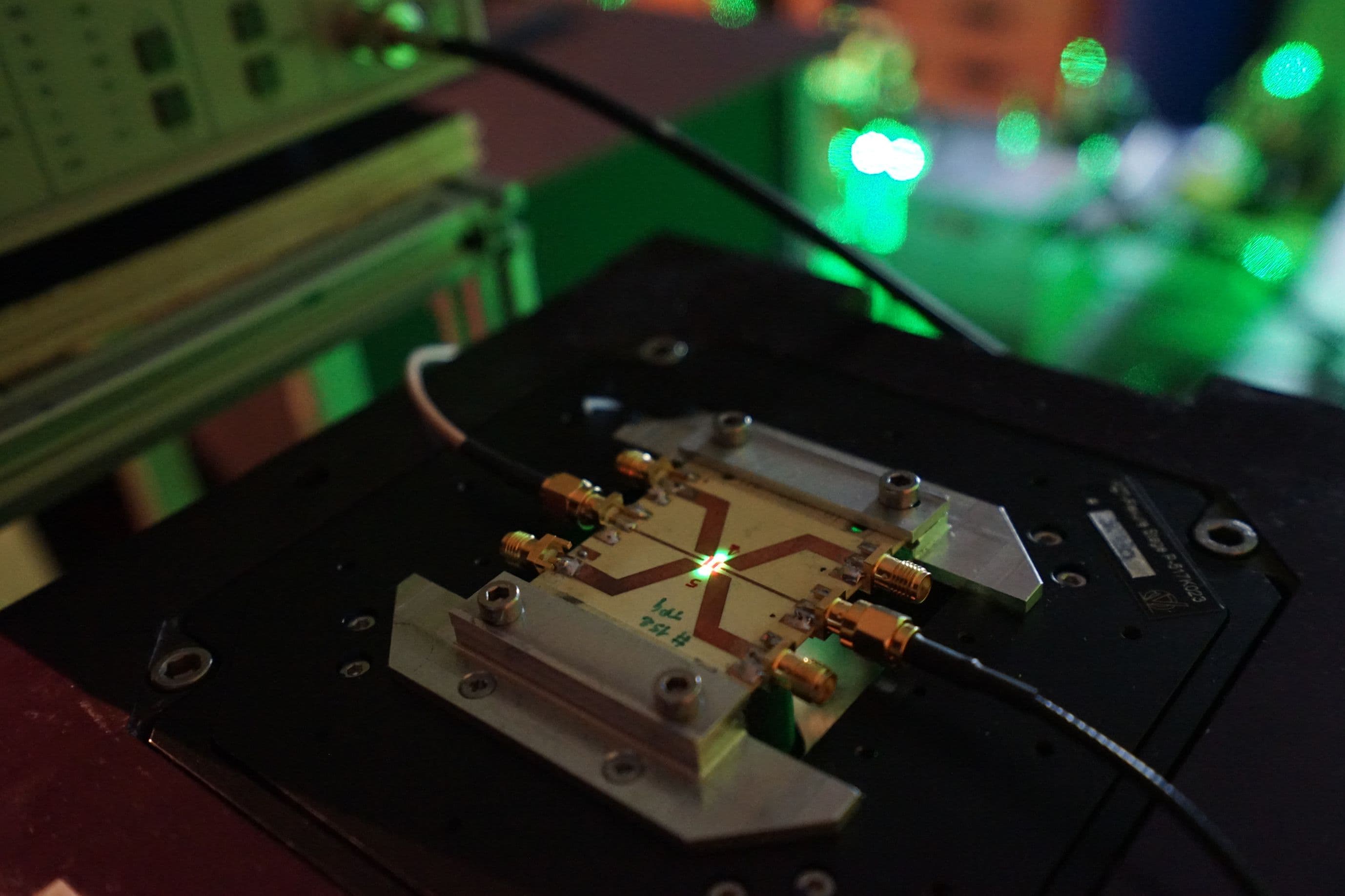 Figure_1_-_Electrically_readable_qubits_0 Diamond quantum device mounted on a microwave board under green laser illumination