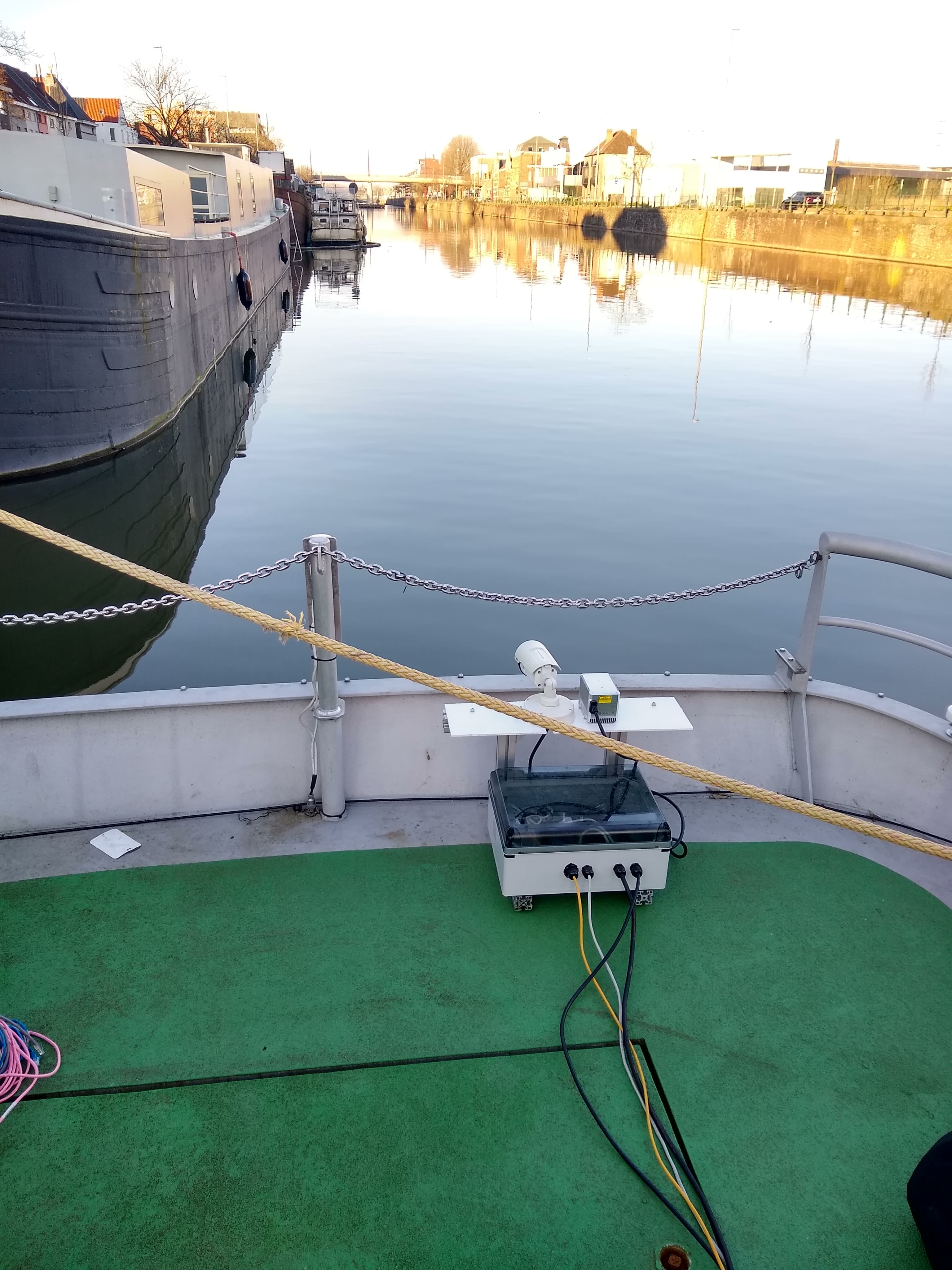 Figuur%203 Sensoren en apparatuur gemonteerd op een bootdek met uitzicht over een kalm kanaal in een haven
