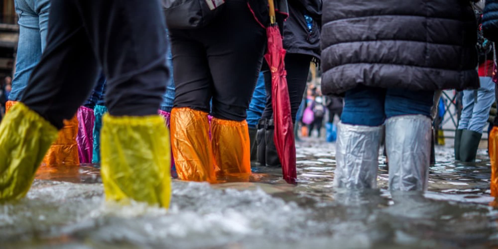 Flooding Mensen staan in hoogwater op een stadsstraat, met kleurrijke waterdichte laarzen aan