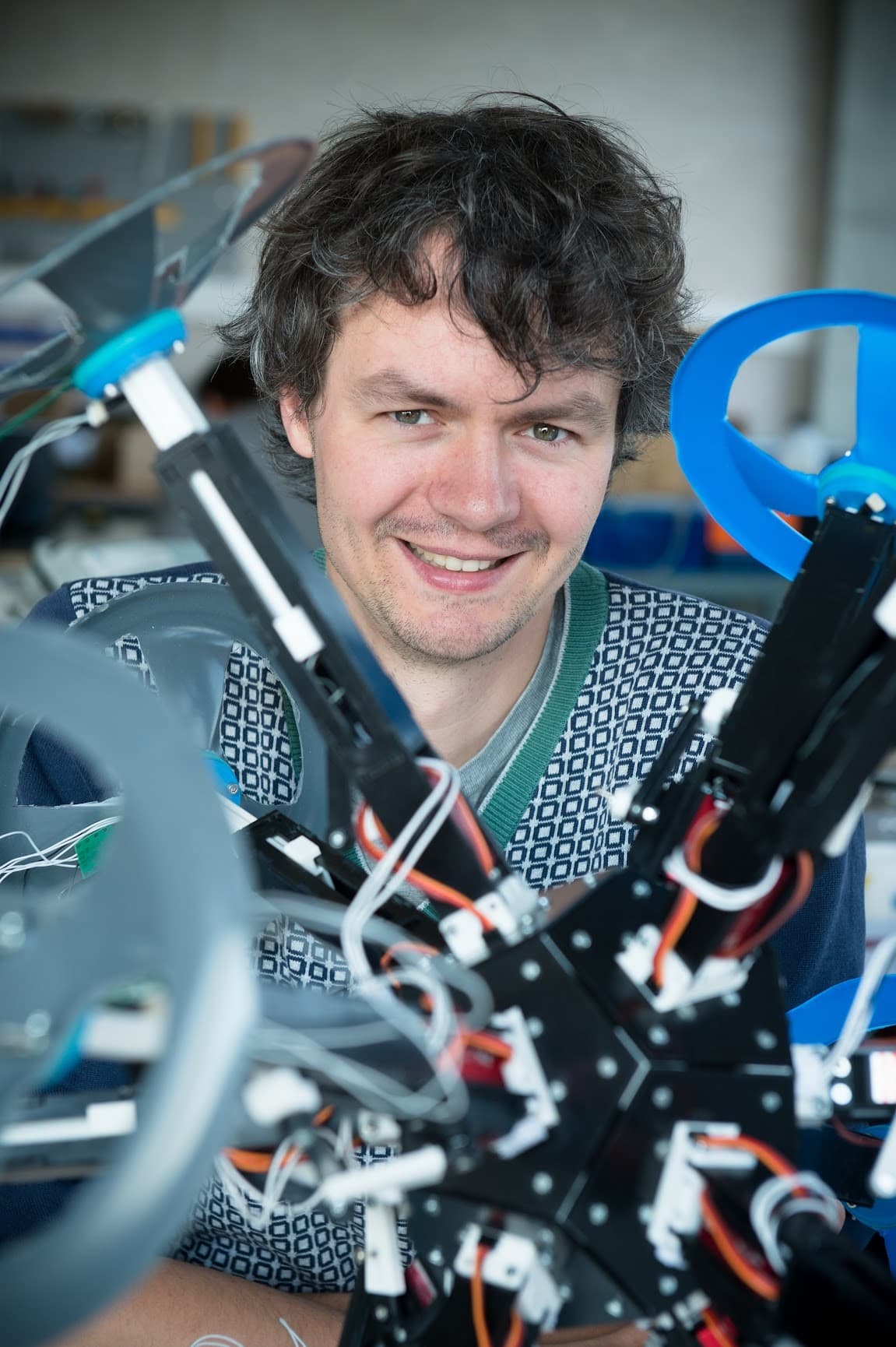 franciswyffels Francis Wyffels glimlachend naast een robot met blauwe cirkelvormige onderdelen en blootliggende bedrading