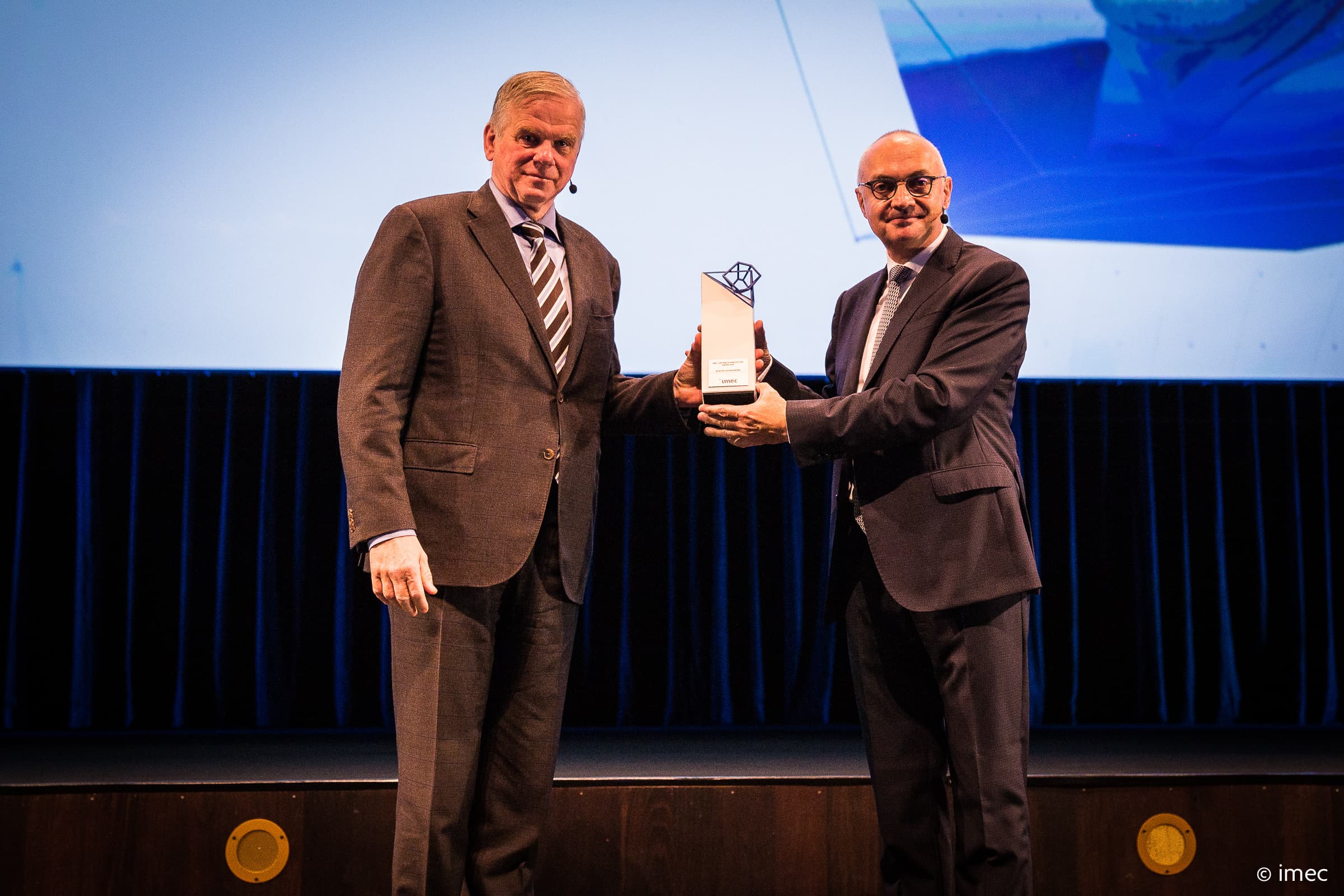 FUTURE_SUMMITS_DAY1-51_1 Two suited men on stage present an Imec Lifetime of Innovation Award trophy