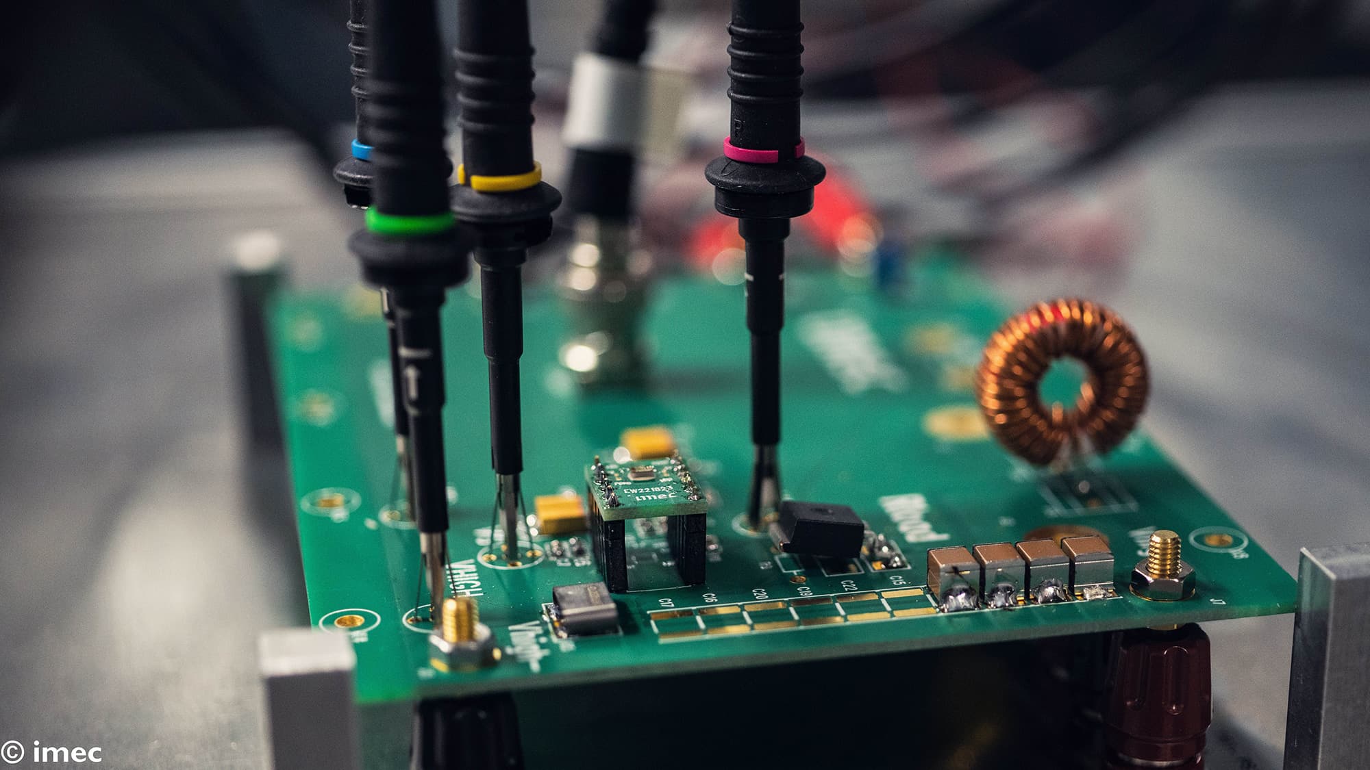 Test probes measuring circuit board in lab Test probes measuring a green circuit board with an inductor and electronic components in a lab setup