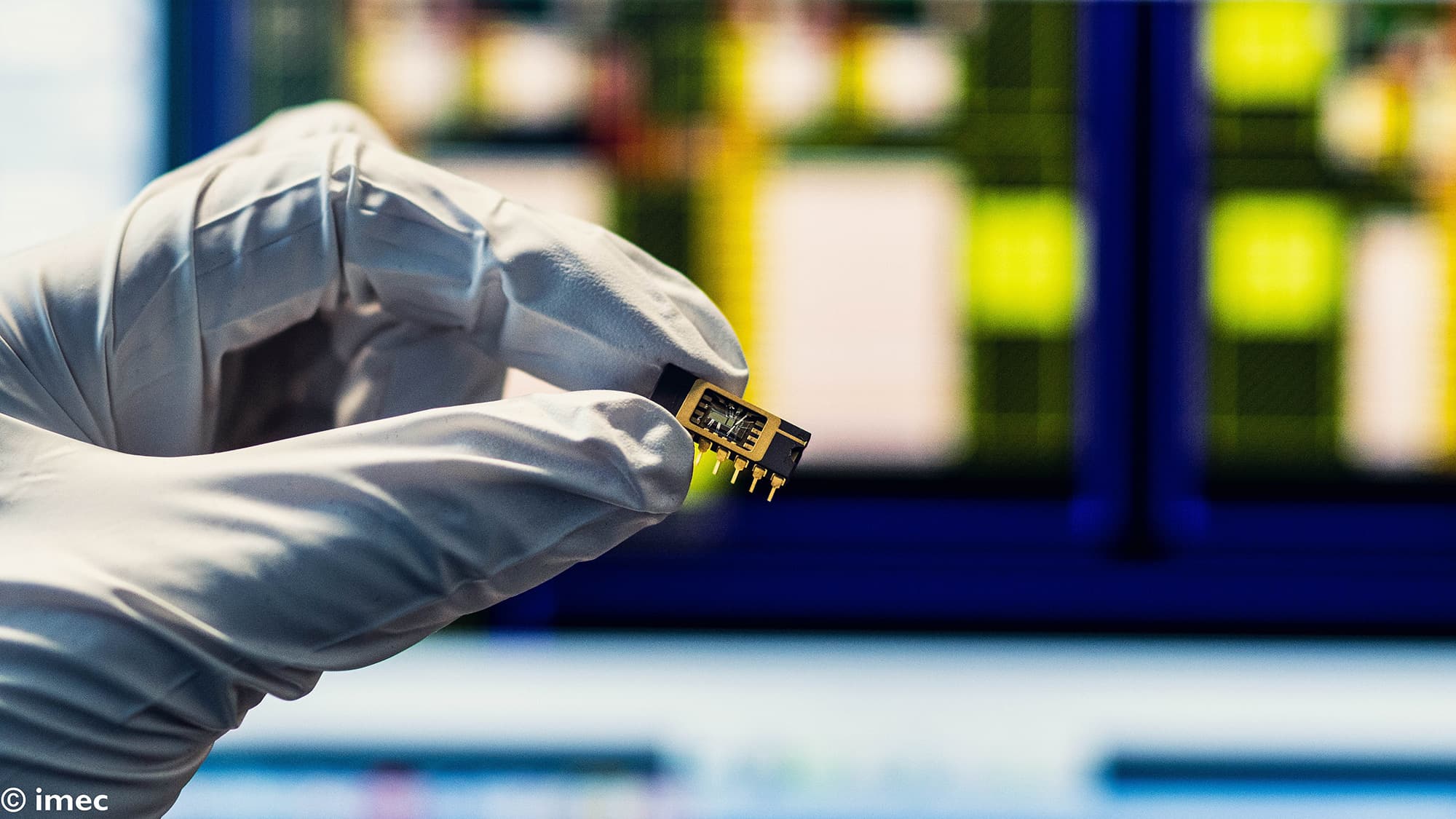 ganic008_low_1 Gloved hand holding a small semiconductor chip package in a lab setting