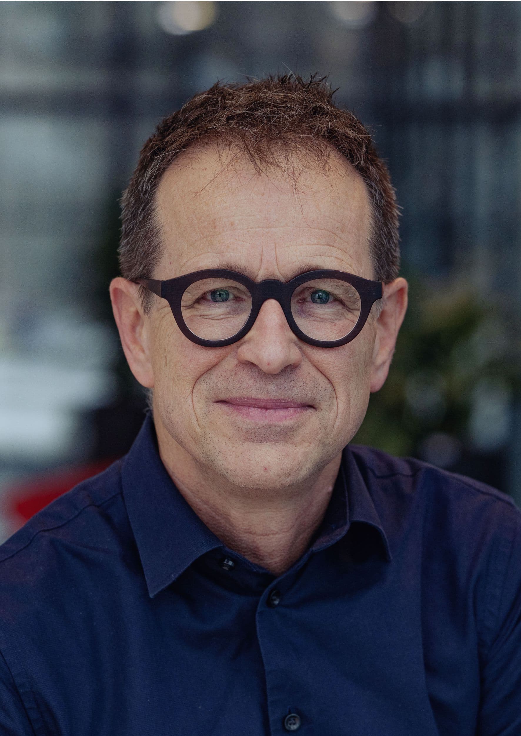 Geert%20Vandenberghe Portrait of Geert Vandenberghe wearing glasses and a dark blue shirt, against a blurred office background.