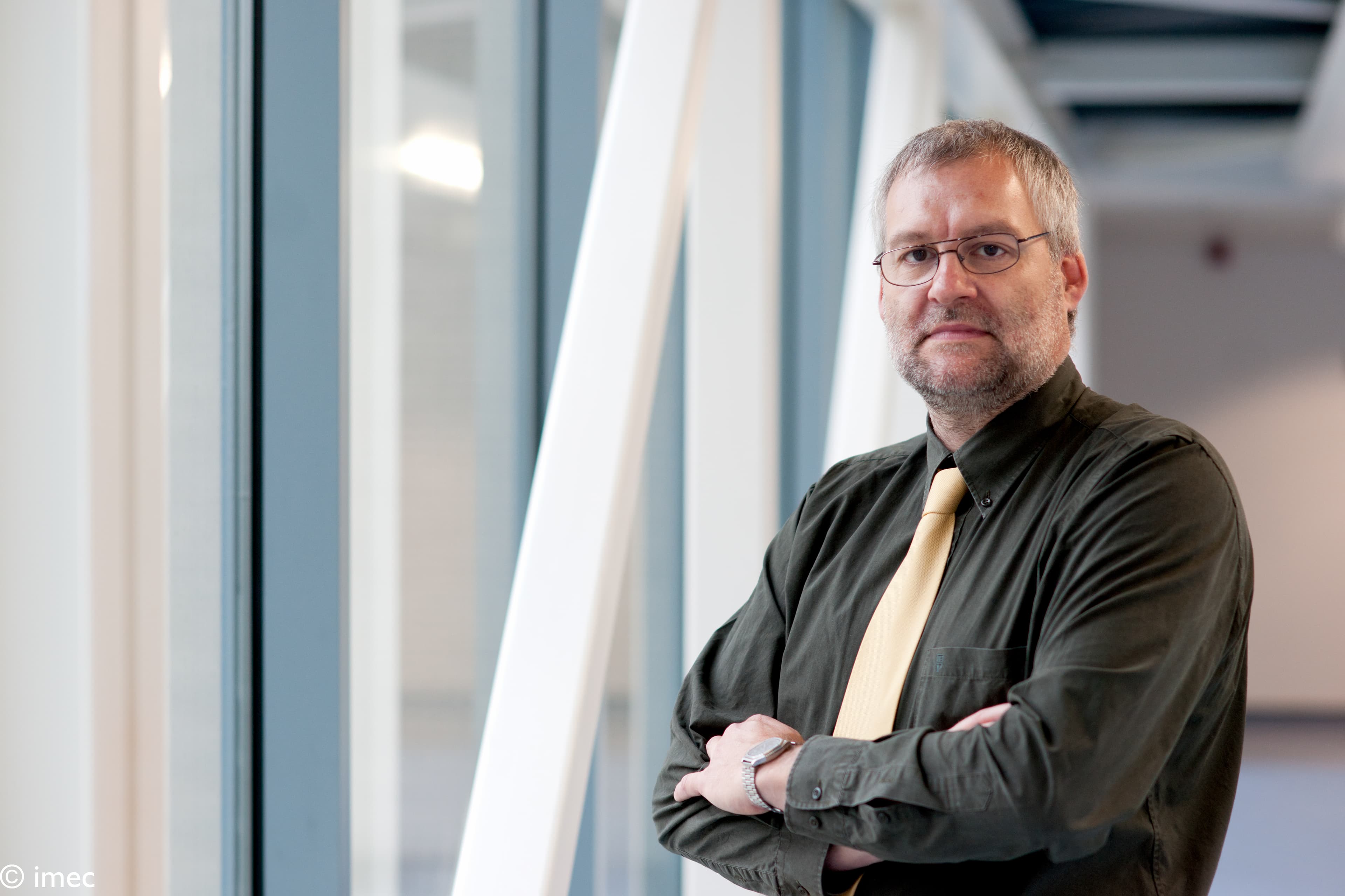 geert_willems_1 Geert Willems standing with arms crossed in a modern office, wearing a black shirt and light tie