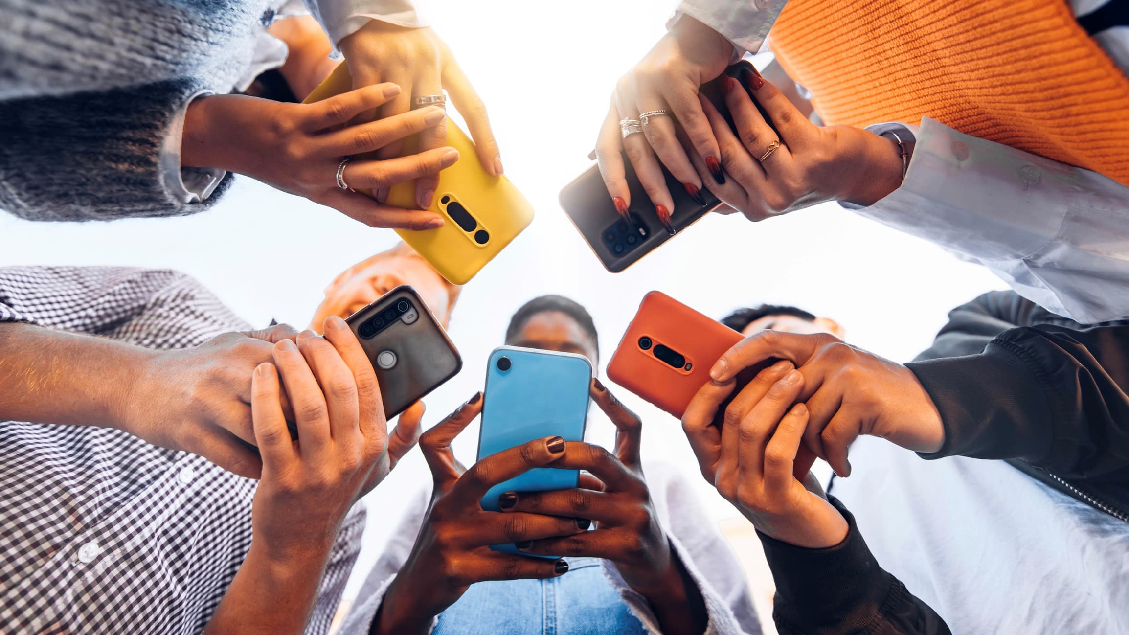 GettyImages-1371958166 Groep mensen die samen smartphones vasthouden in een cirkel, van onderen gezien