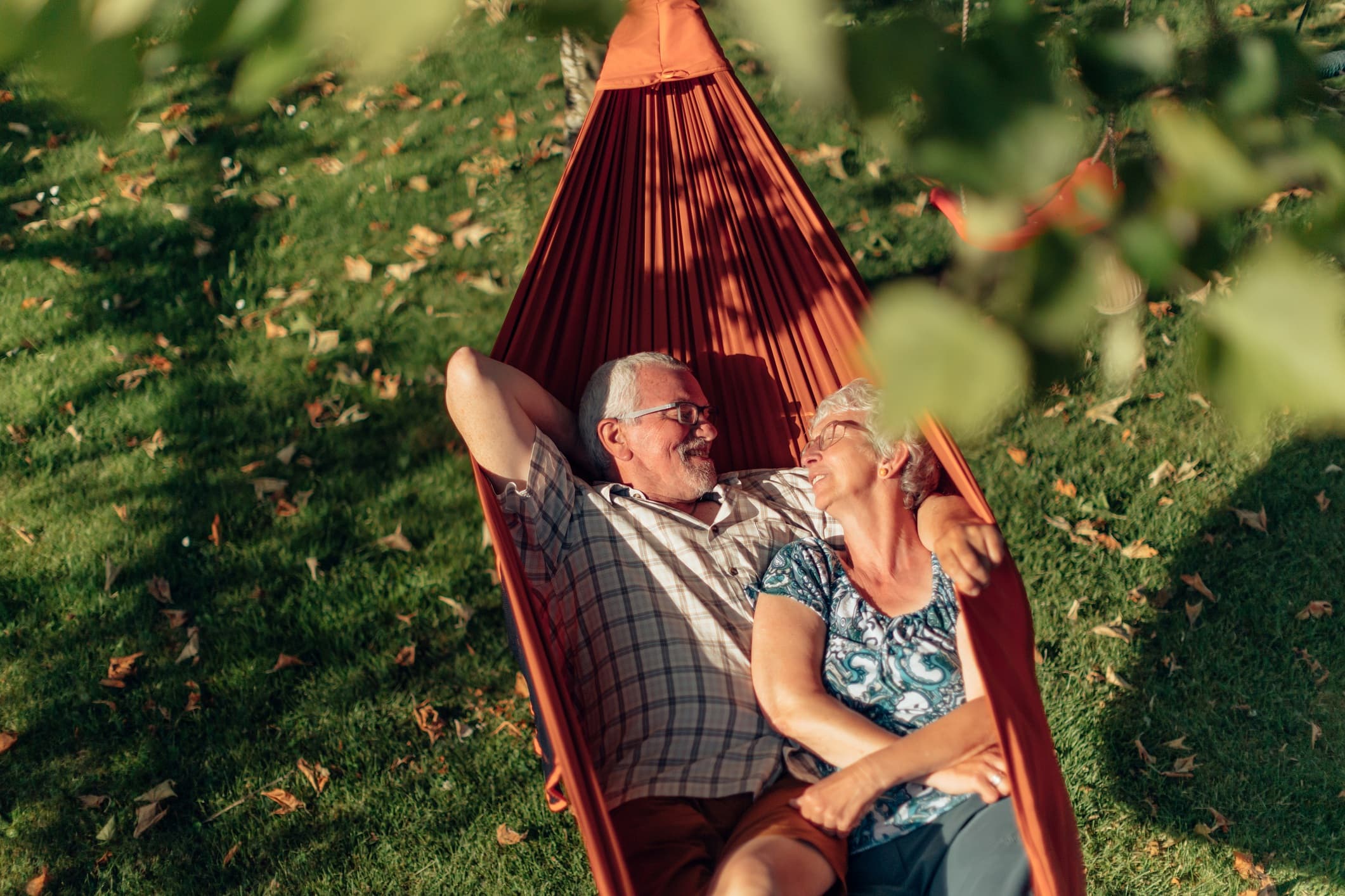 GettyImages-1478050224 Een ouder stel ontspant samen in een oranje hangmat op een grasveld.