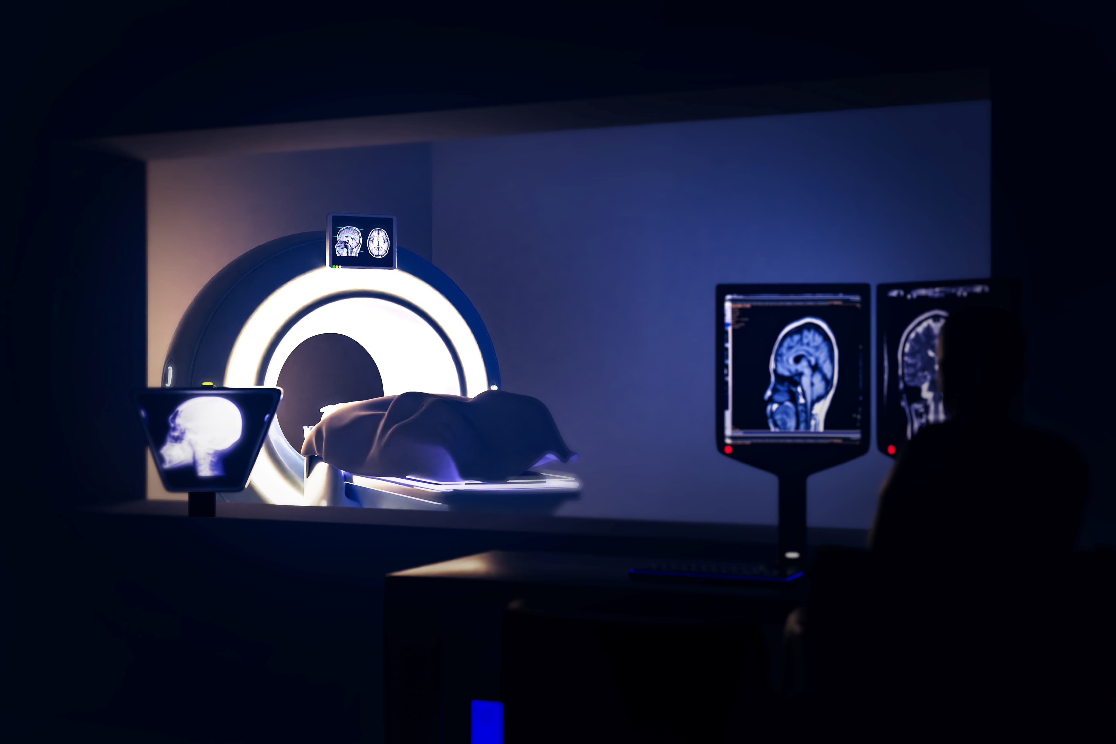 GettyImages-1575401538 MRI-scanner met hersenscans op nabijgelegen monitoren in een schemerig verlichte kamer