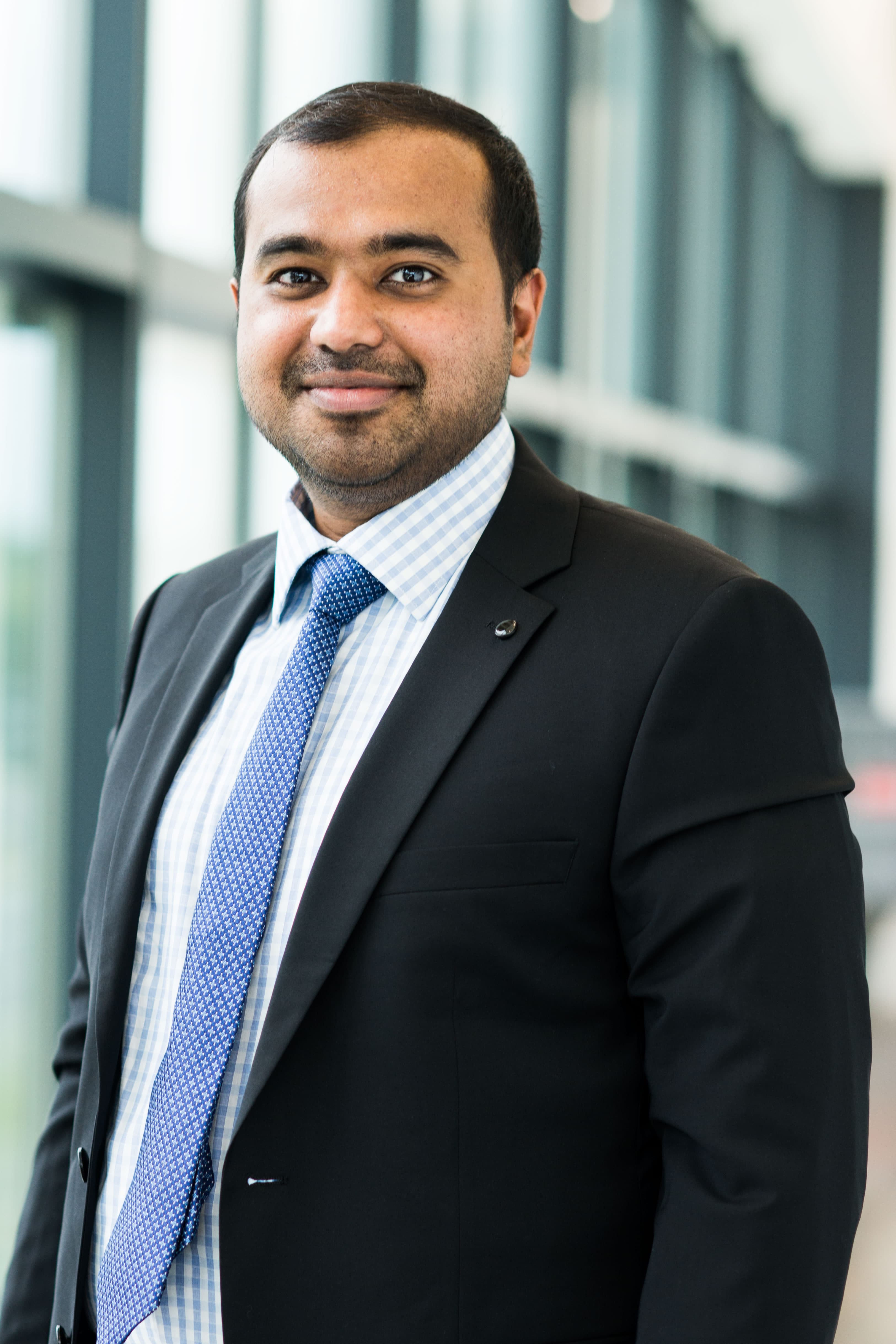 Hariharsudan-Sivaramakrishnan-Radhakrishnan003 Portret van een man in een pak en blauwe stropdas, glimlachend binnen.