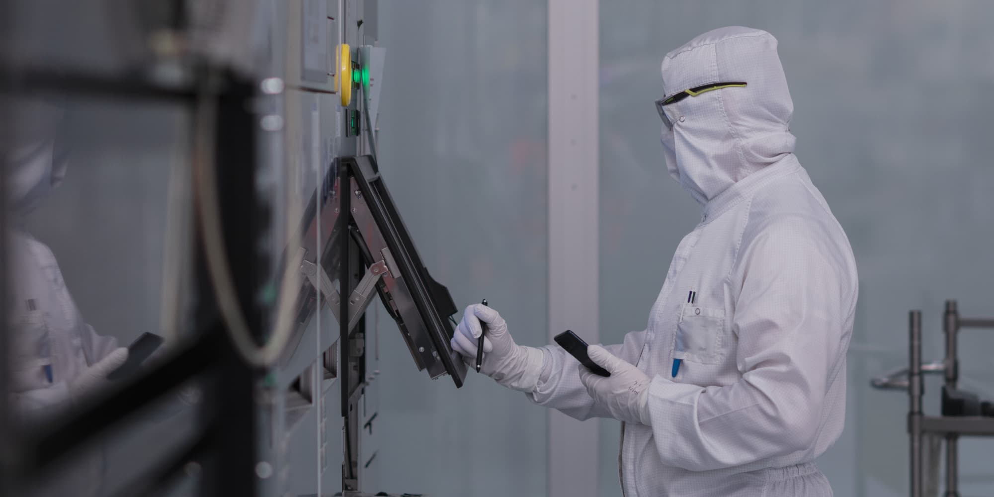 header-cleanroom_0 Cleanroom worker in protective suit operating equipment with a handheld device.