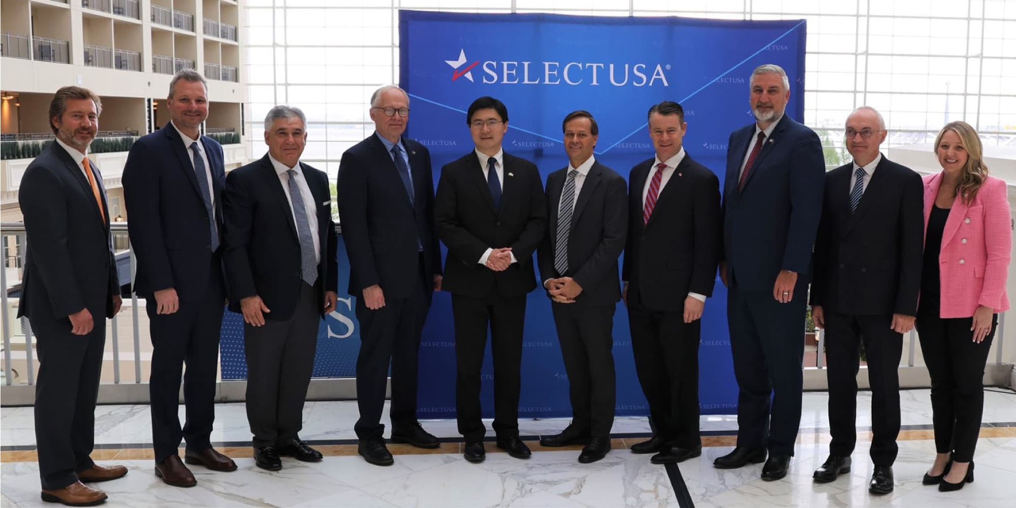 header-MOU_0 Group of officials posing for a partnership photo in front of a SELECTUSA backdrop.