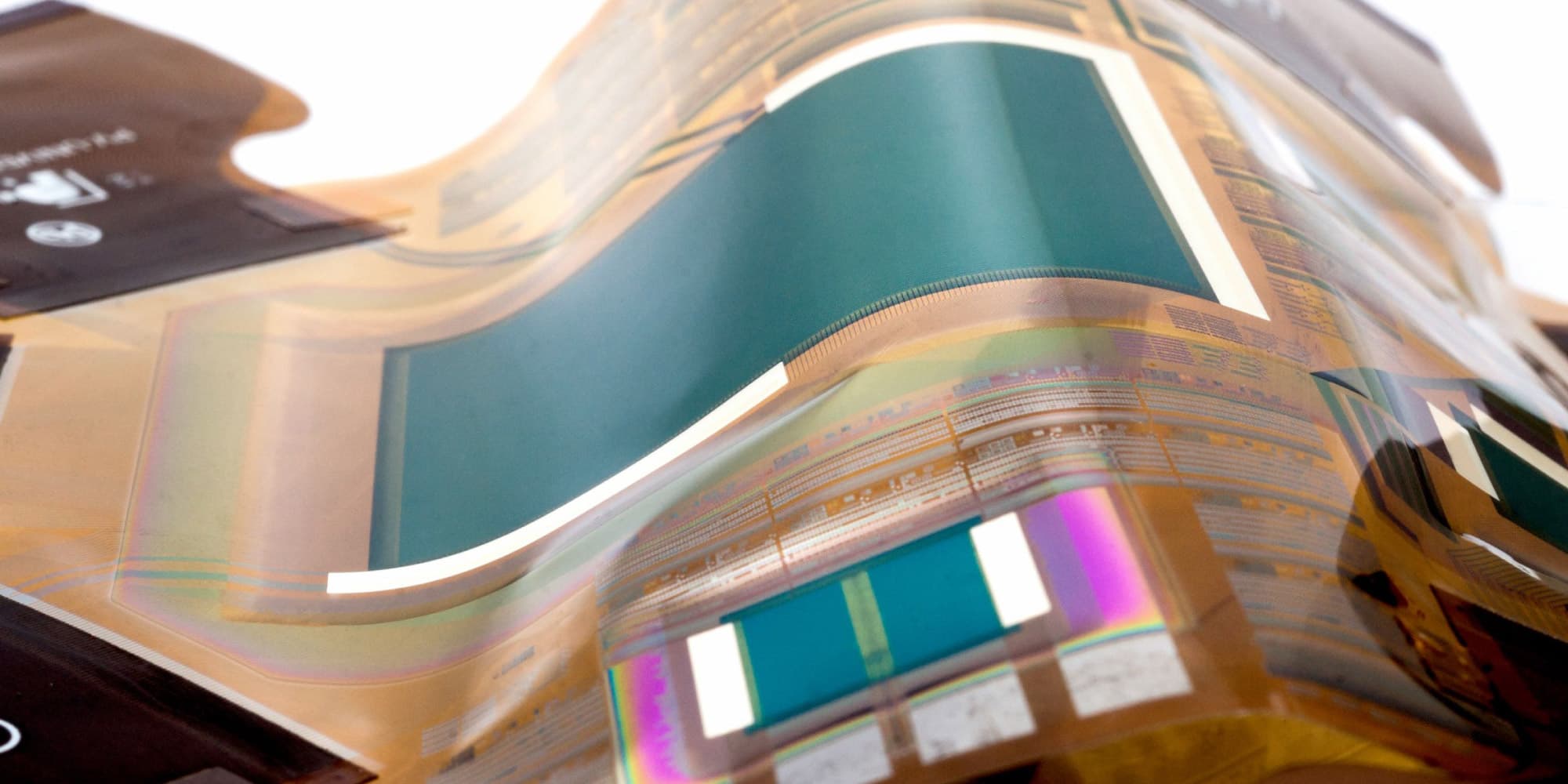 header_thin-film-transistor Close-up of a flexible thin-film transistor wafer with colorful reflective circuitry patterns