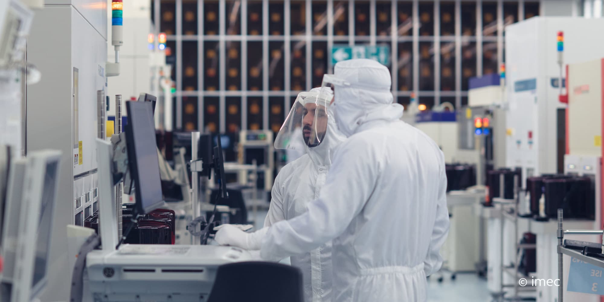 Header-VLSI Two researchers in cleanroom suits working at equipment in a semiconductor lab