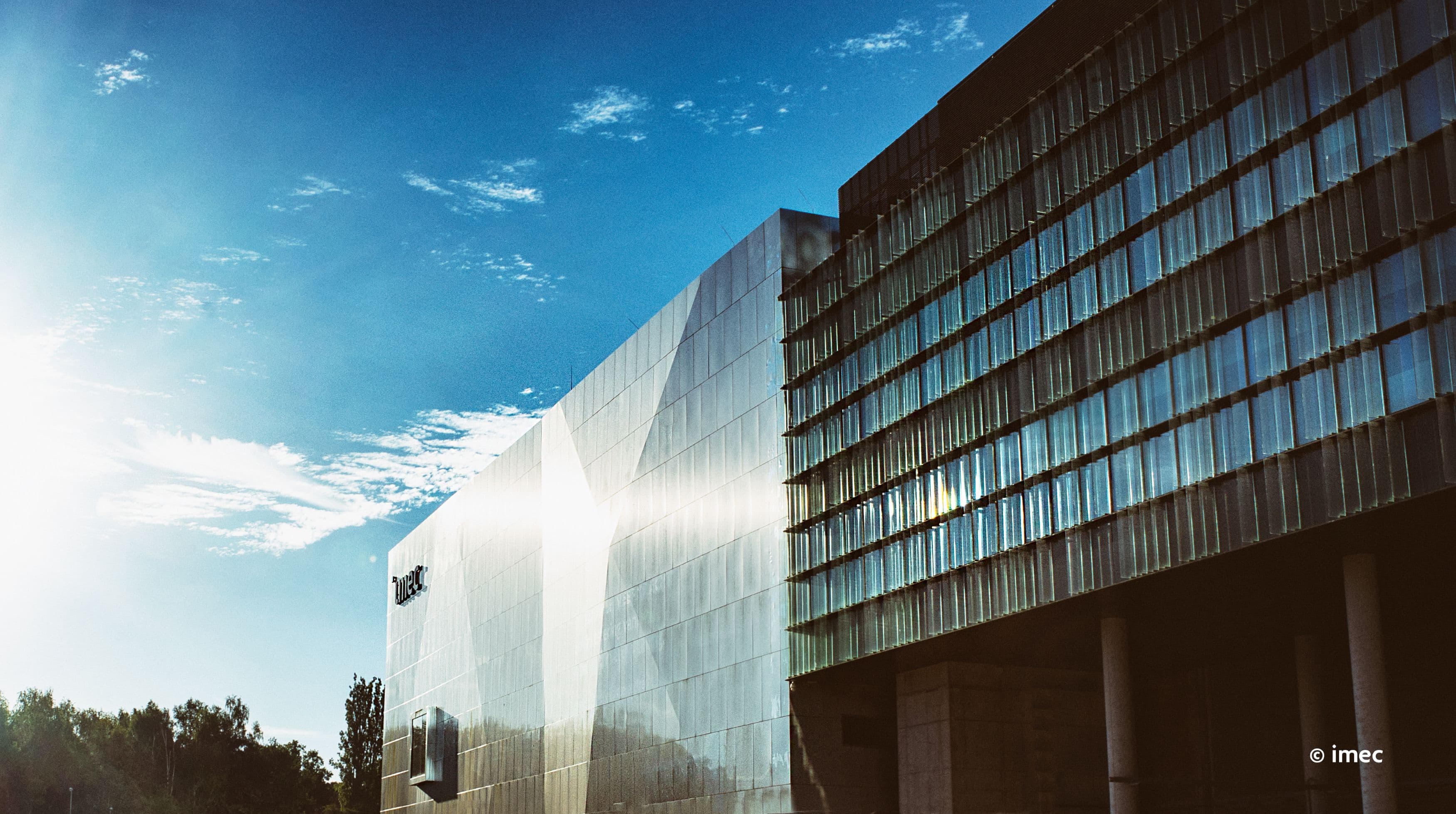 header Imec building exterior under a blue sky with sunlight reflecting off the facade
