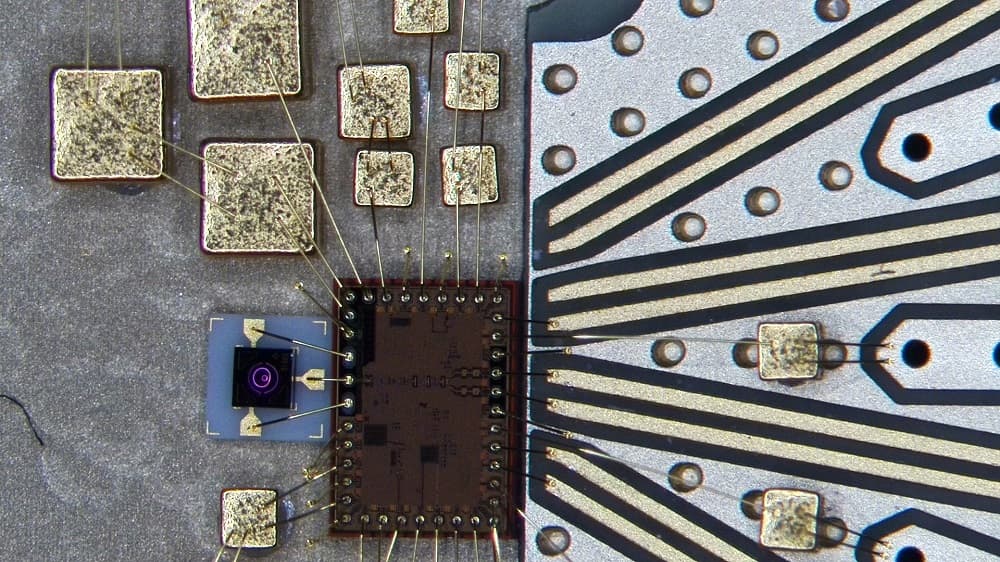 Microchip and bonded wire connections with optical sensor Microchip and bonded wire connections on a circuit board next to a small optical sensor