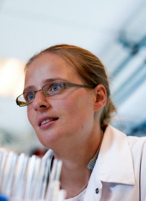 hilde_jans_portret_1 Portrait of Hilde Jans in a lab coat and glasses, looking upward in a laboratory setting