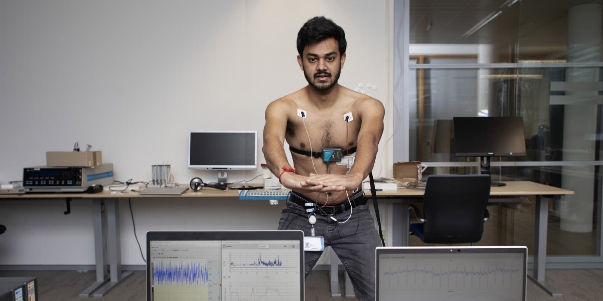Hoe-een-nieuwe-generatie-wearables-de-gezondheidszorg-transformeert Onderzoeker met lichaamssensoren en borstmonitor in een lab, met hartslaggegevens op laptops op de voorgrond