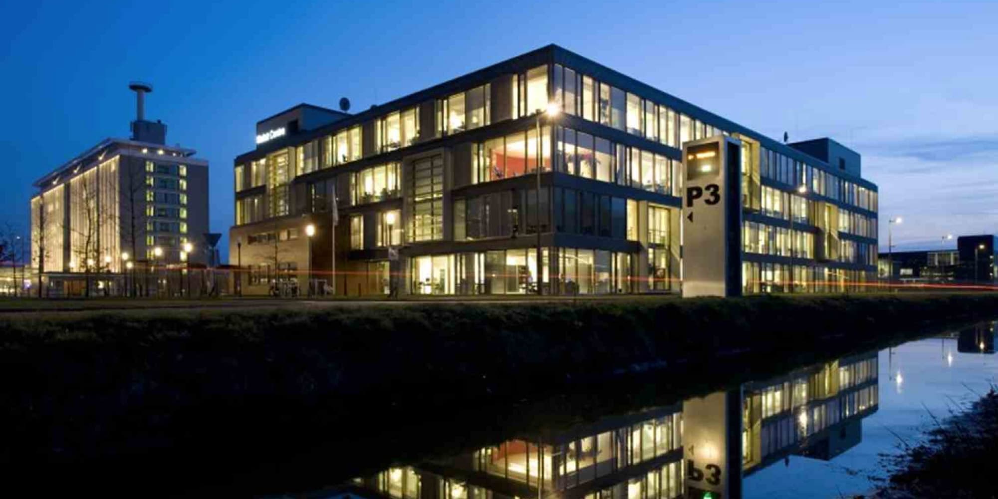 Holst Holst Centre building at dusk, lit windows reflected in a canal