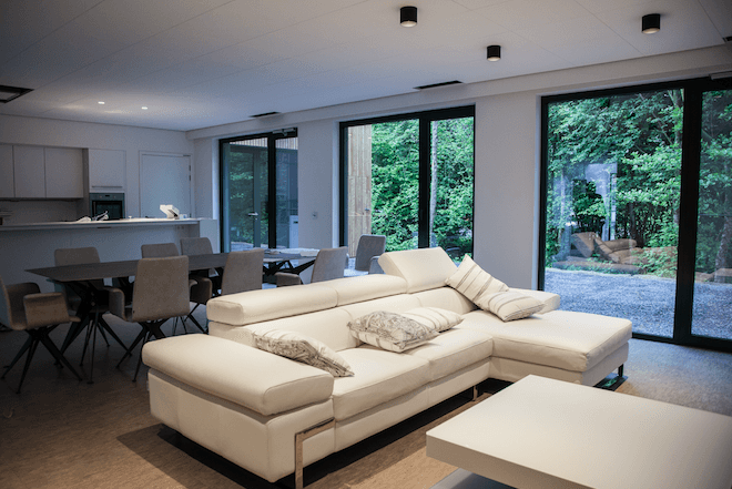 HomeLab_Interior Modern HomeLab-interieur met witte hoekbank, eettafel en grote ramen met uitzicht op groen