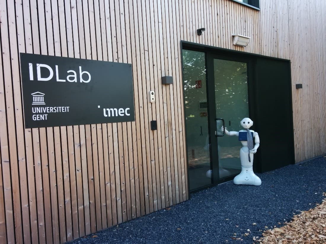 HomeLab Ingang van IDLab met borden van imec en Universiteit Gent, en een humanoïde robot die bij de deur staat