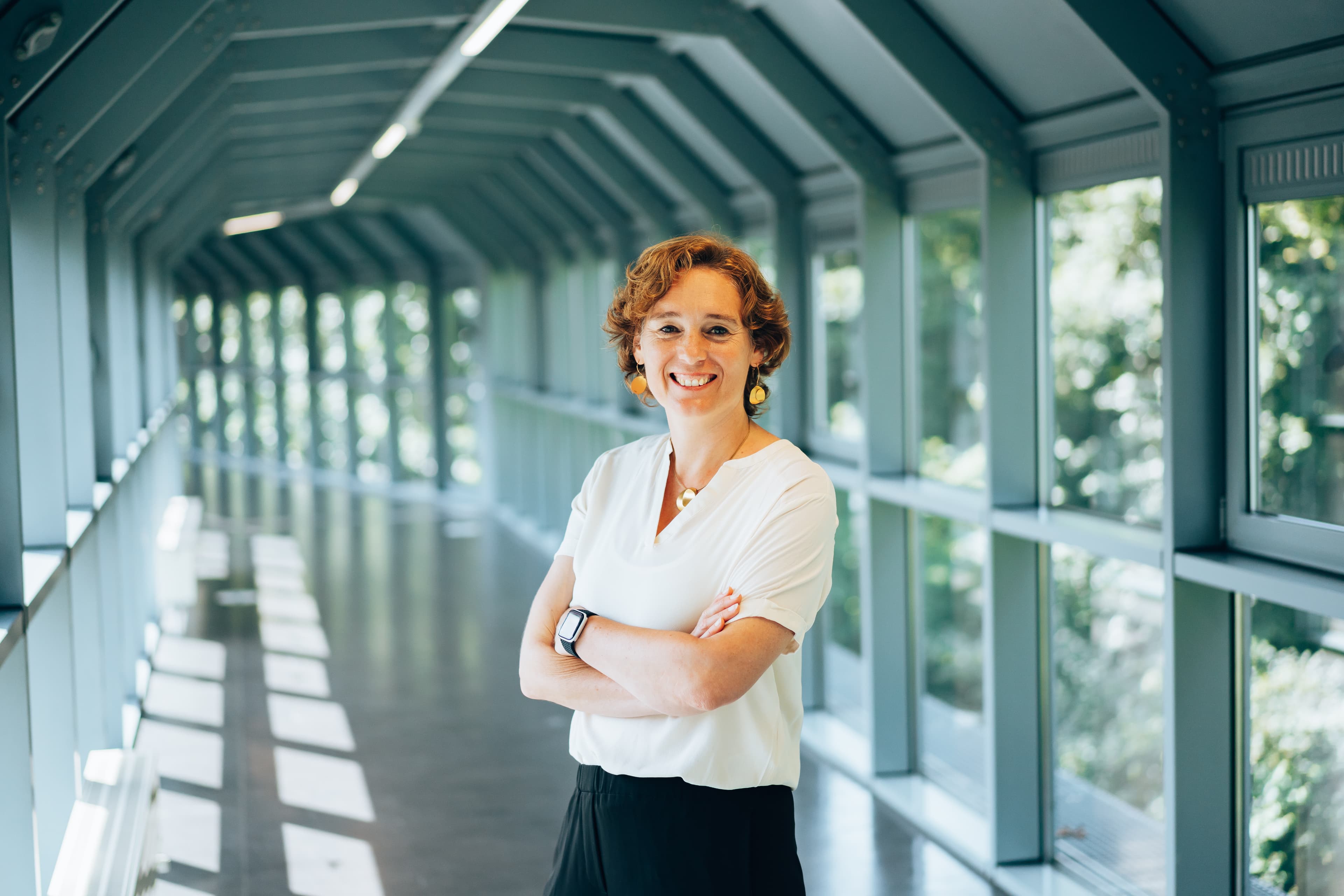 Ilse%20Ooghe-26 Portret van Ilse Ooghe, staand met gevouwen armen in een lichte gang