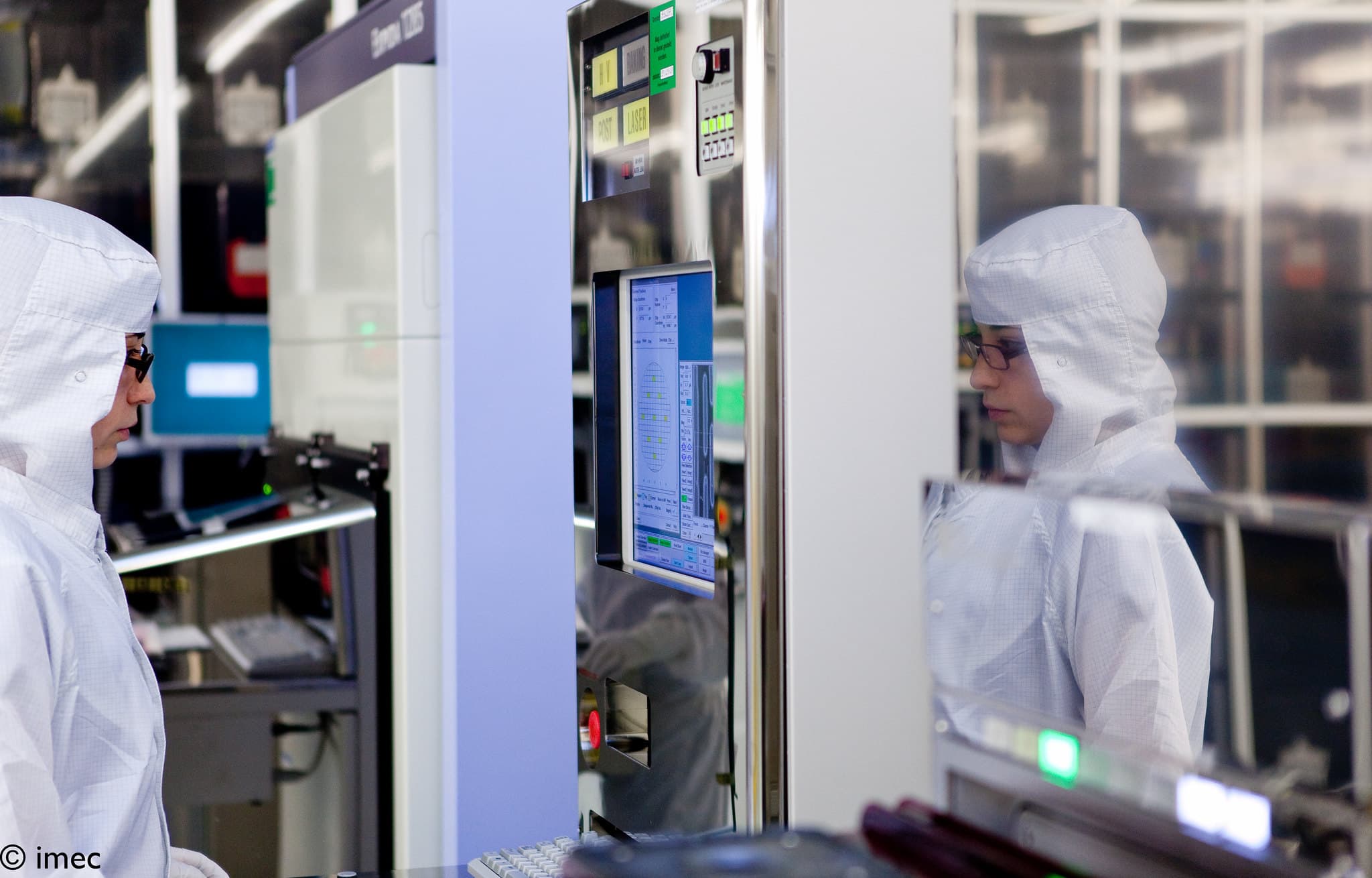 Imaging%20technology Cleanroom researchers in white suits inspect a semiconductor machine with a control screen