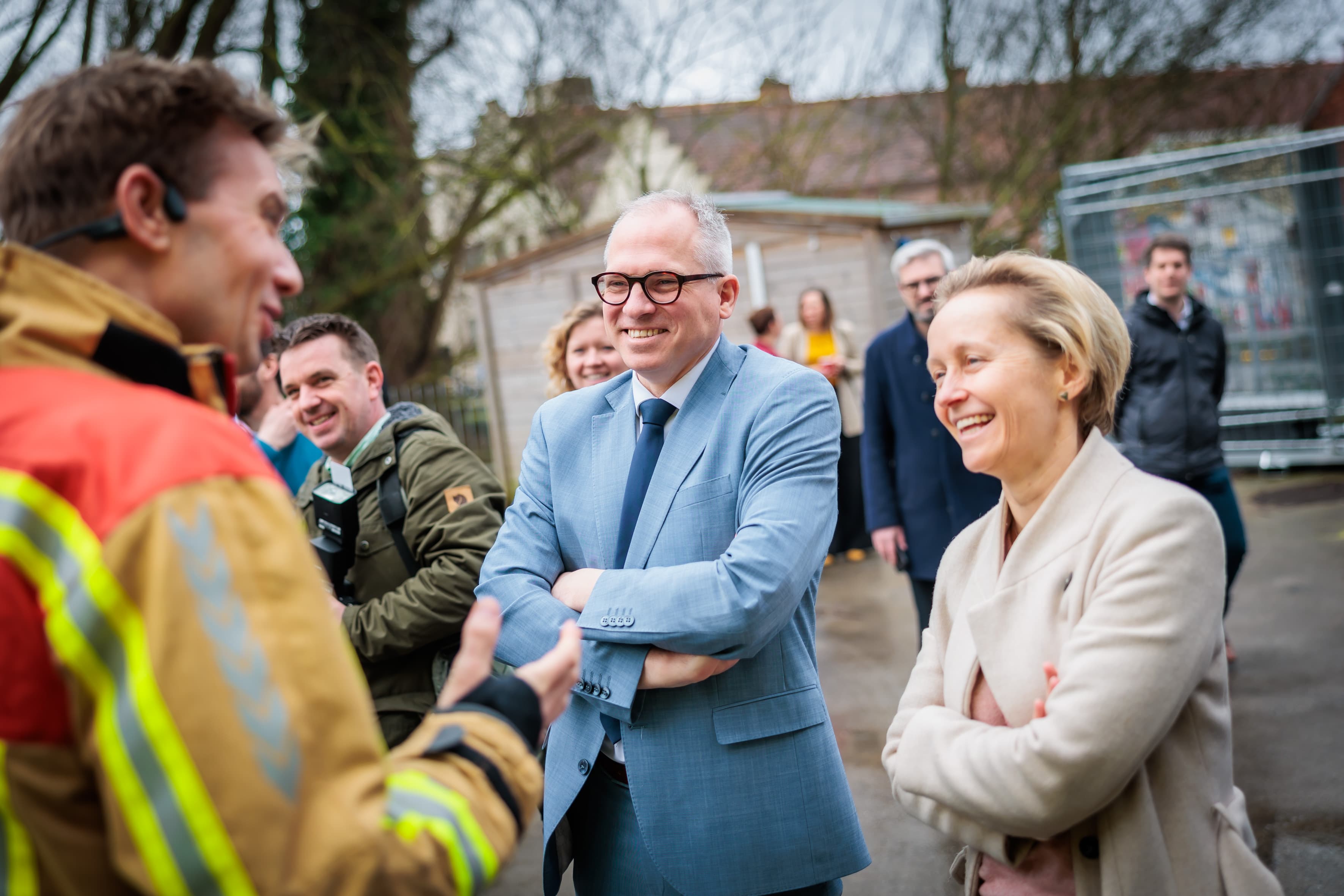 Imec-188MD%20en%20ADR Een brandweerman in reflecterende kleding spreekt buiten met glimlachende functionarissen