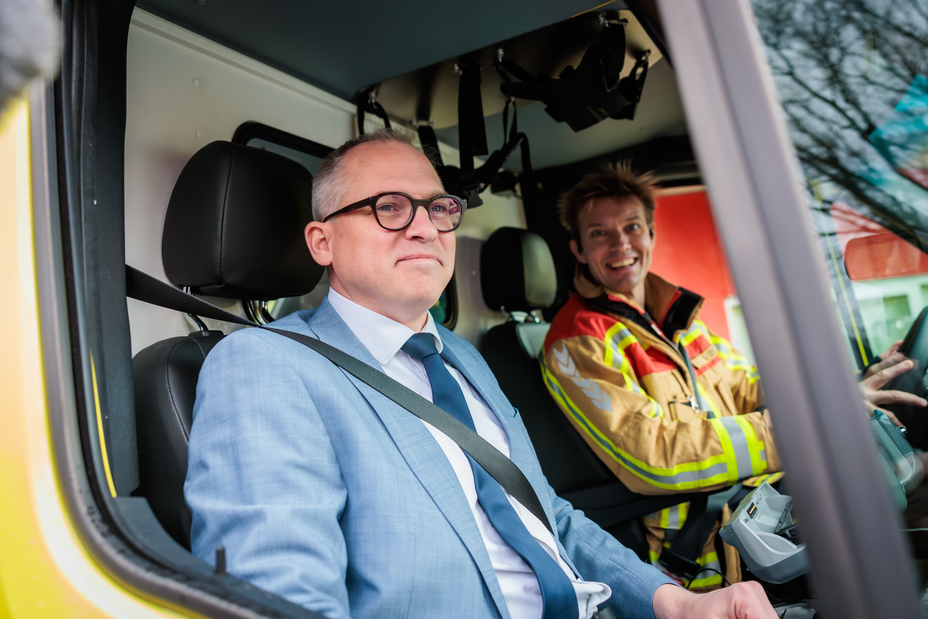 Imec-202MD Twee mannen zitten in de cabine van een hulpvoertuig, een in pak en een in brandweeruitrusting